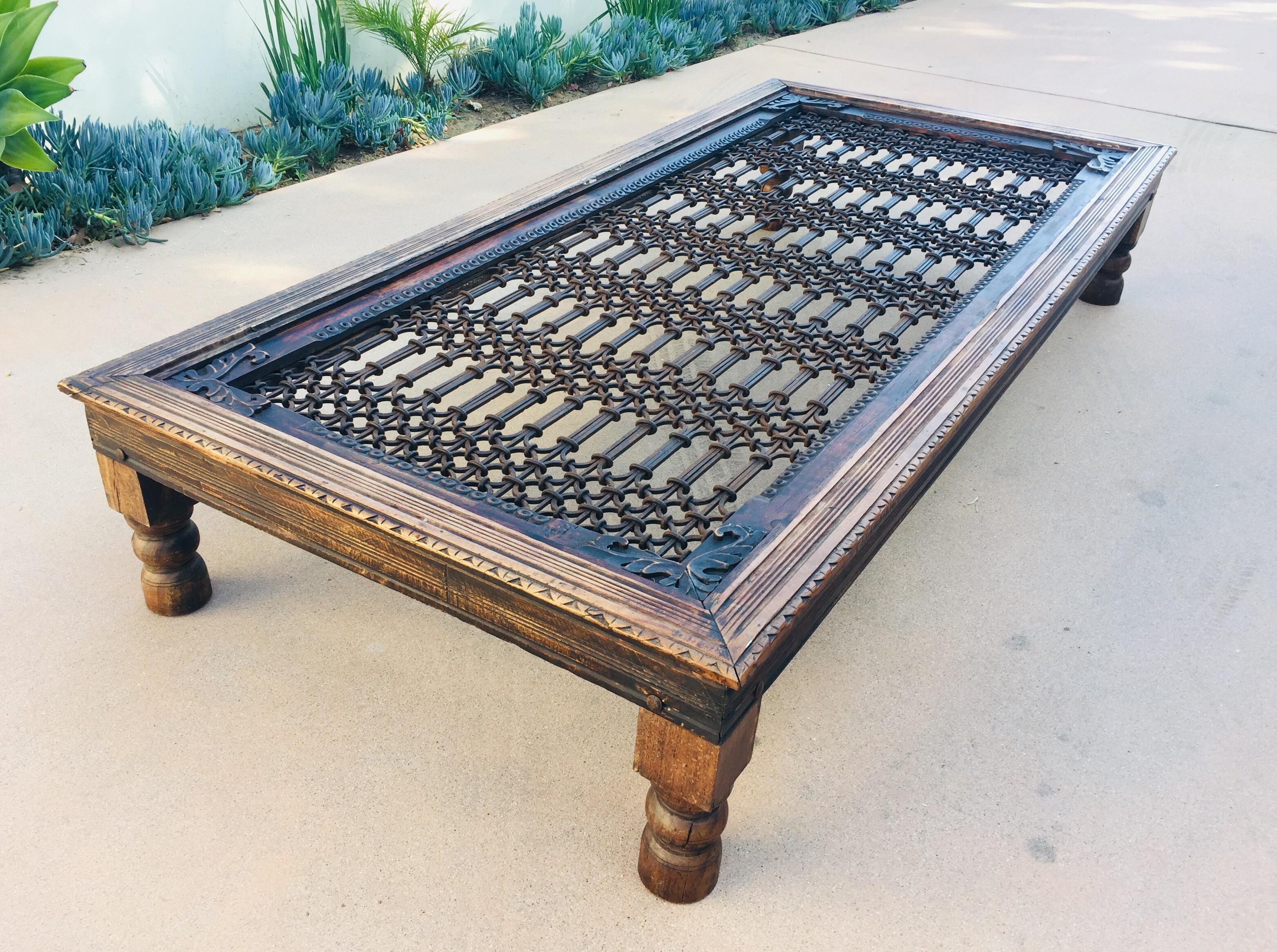 Teak wood coffee table with iron inset jail work.
Large coffee table in solid teak wood with nail heads and metal iron work, very nicely carved legs and sides. 
Antique architectural window screen from India made into a table. 
The hand forged solid