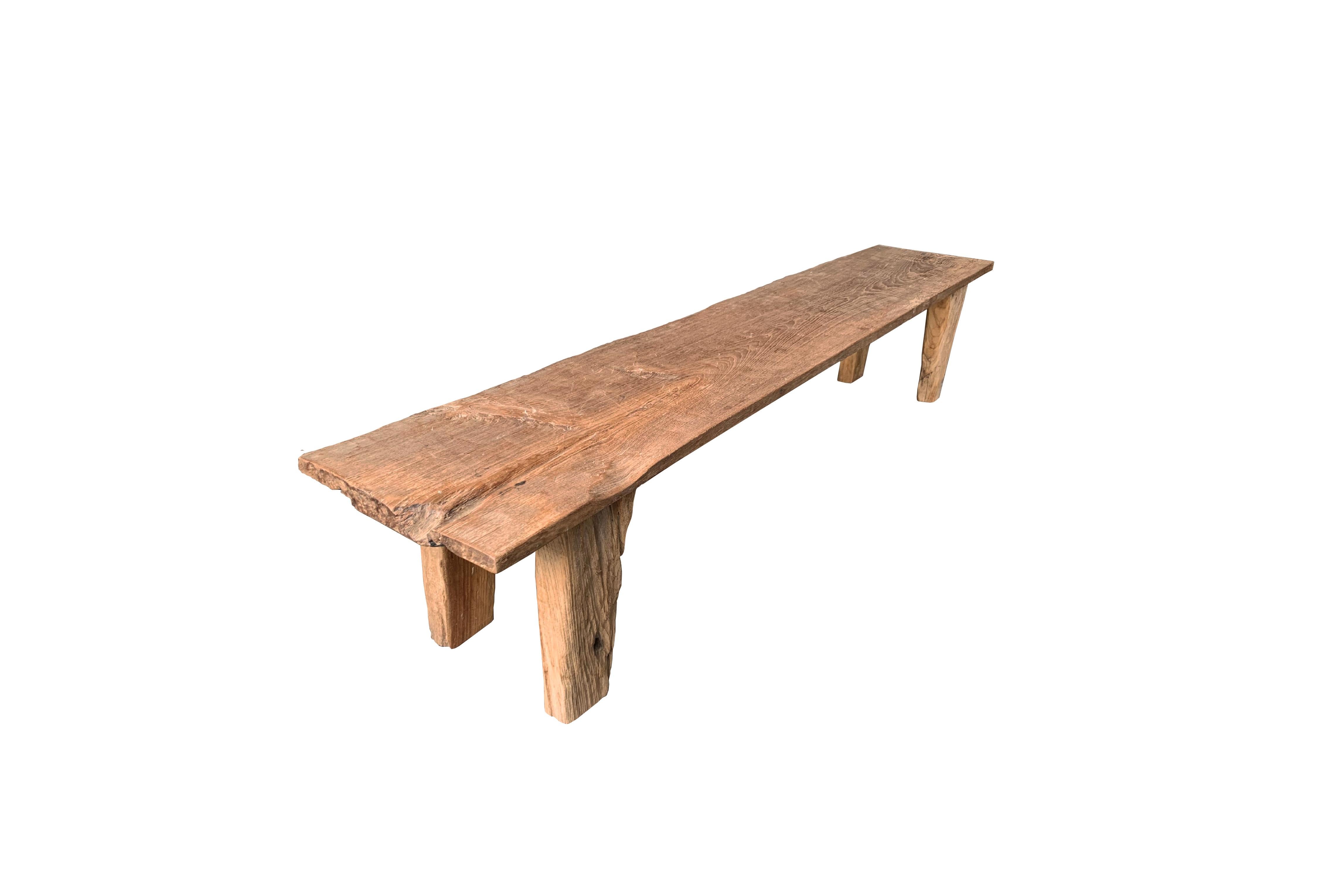This teak wood bench originates from the Island of Madura, off the coast of Northeastern Java. It features a wonderful organic form with a mix of wood textures and shades. Elevated by four solid, angular legs, the seat was carved from a single block