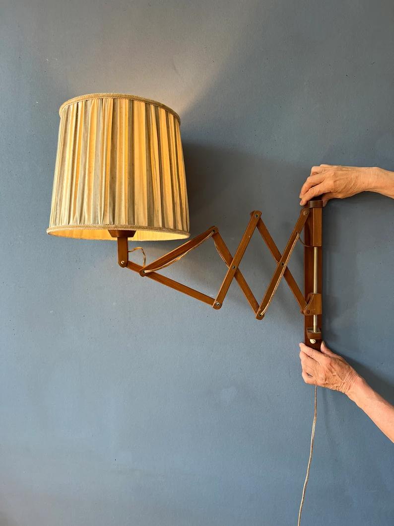 Danish scissor lamp with wooden frame and beige shade. The scissor-mechanism allows you to extend the lamp from the wall. The shade can be adjusted too. The lamp requires an E27/26 (standard) lightbulb and currently has an EU-plug.

Additional