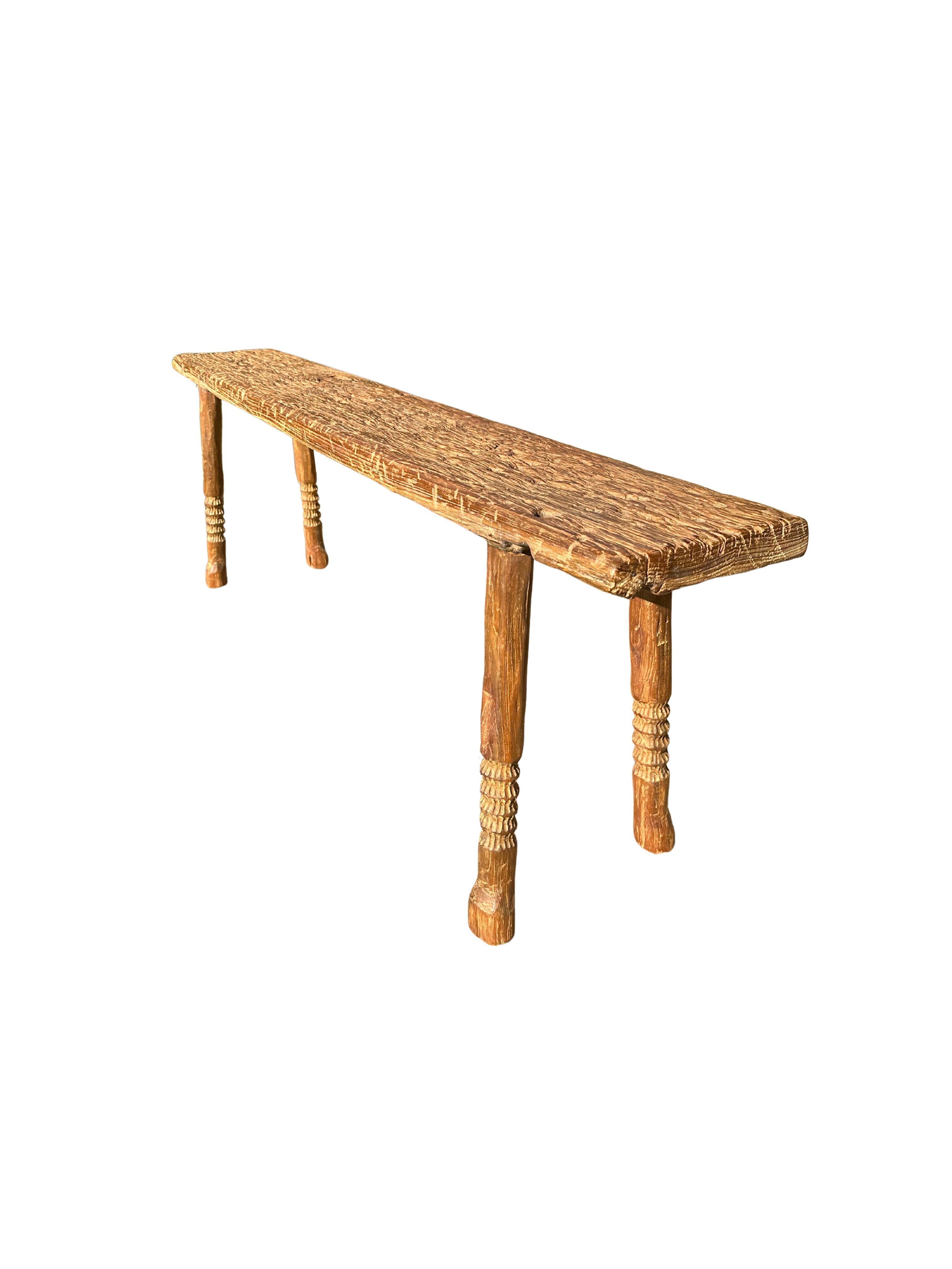 Un banc en teck merveilleusement sculptural avec des détails sculptés sur l'assise. Ce banc en bois de teck présente une merveilleuse forme organique avec un mélange de textures et de nuances de bois. Surélevé par quatre pieds élancés en teck, le