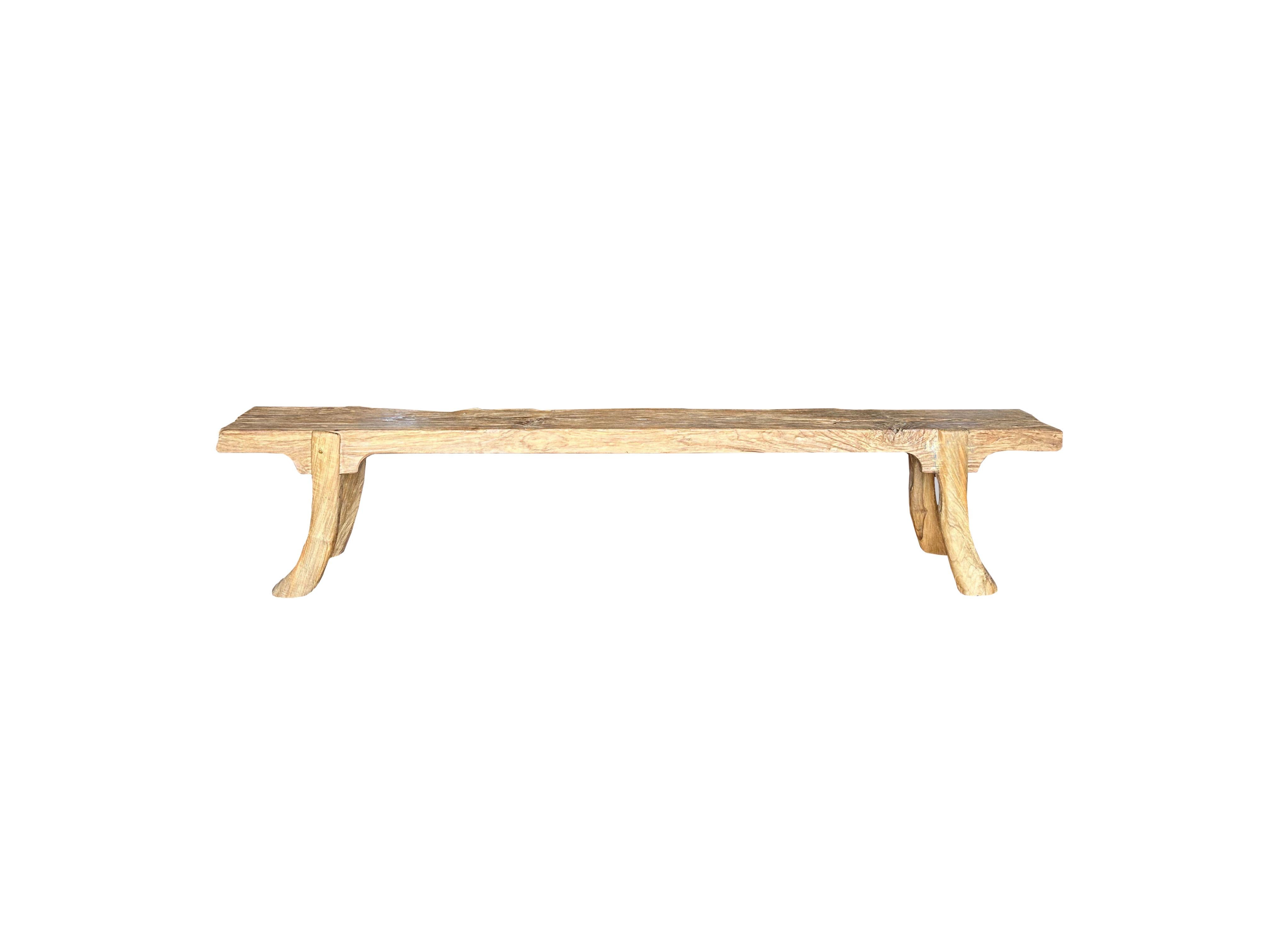 A wonderfully sculptural teak wood bench. This teak wood bench features a wonderful organic form with a mix of wood textures and shades. Elevated by four slender teak wood legs, the seat was carved from a single block of wood. Carved by artisans on
