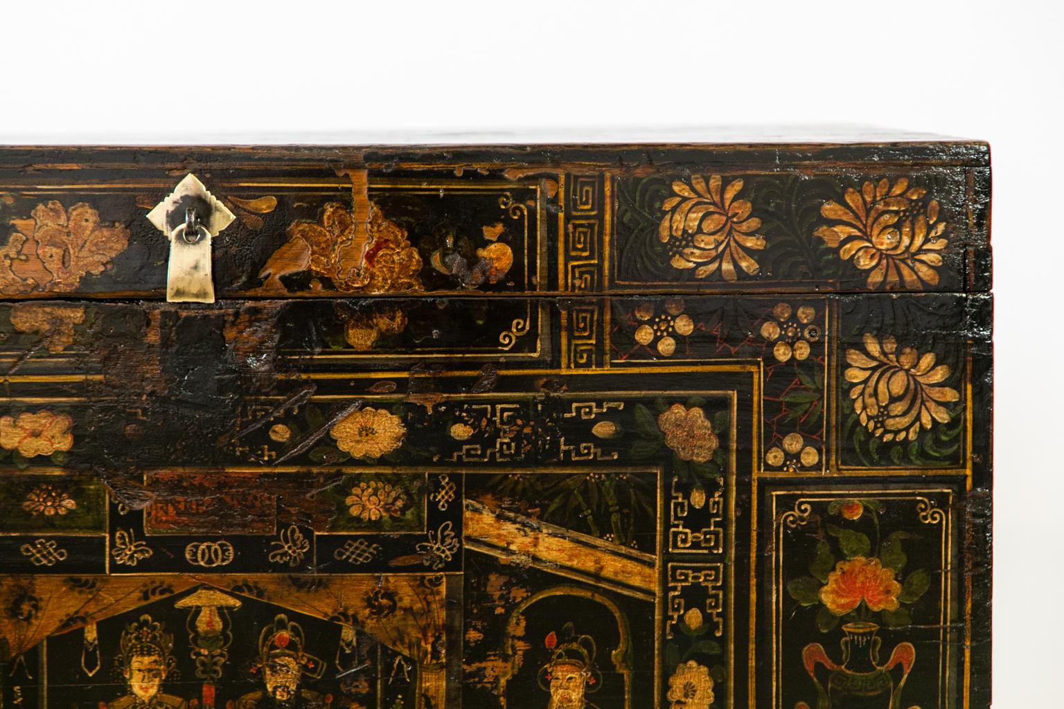 Teakwood Chinese Painted Storage Trunk has the original steel hinges with some replacement screws. The painting depicts floral designs with vases, flowers, and mandarin figures at a table having tea with attendants standing in an adjacent doorway.