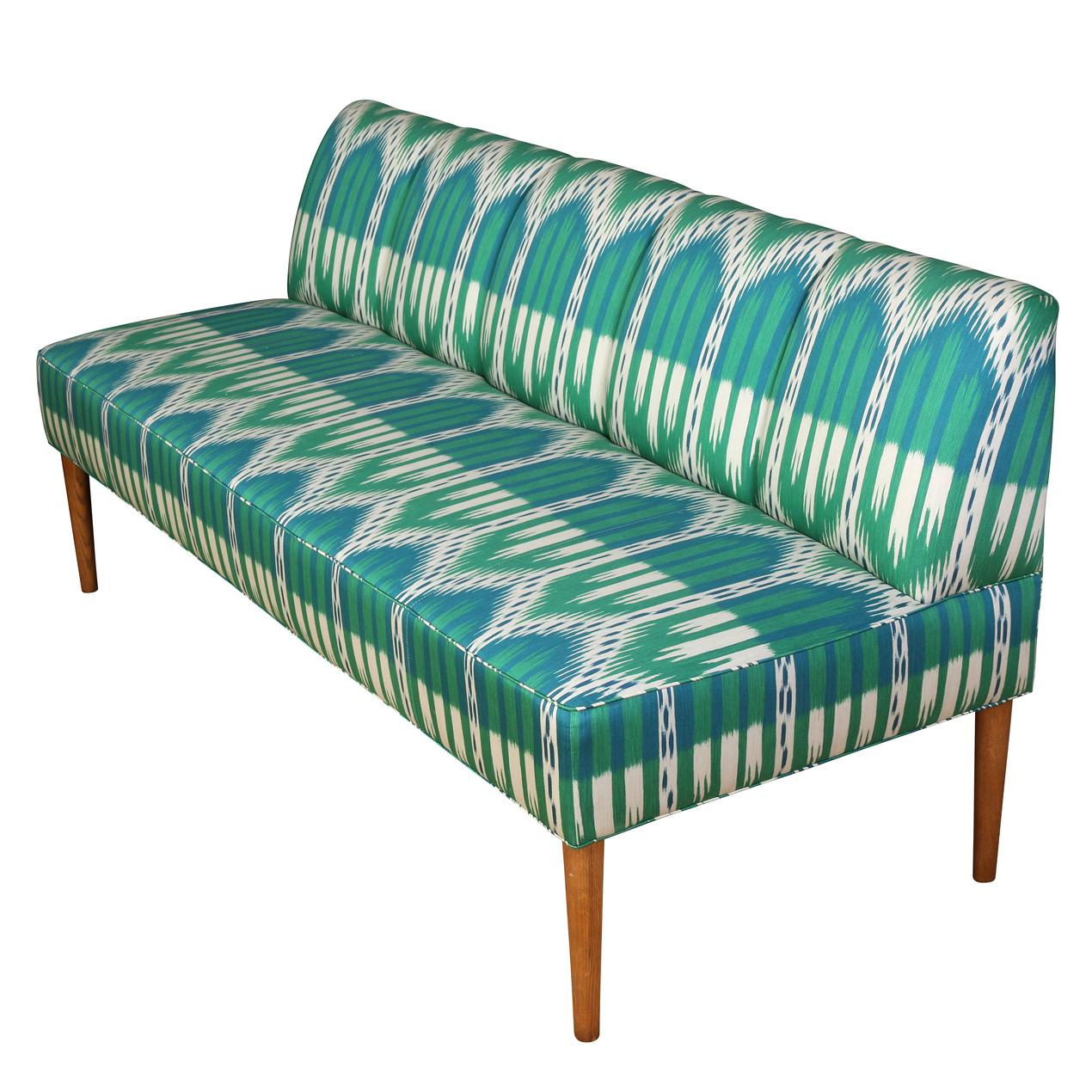 A teal and turquoise ikat upholstered banqette adds a happy punch of color to a room.  The chic bench seating in vibrant blues and greens has a channel back and self welt bench seat with slender and tapered wood legs.