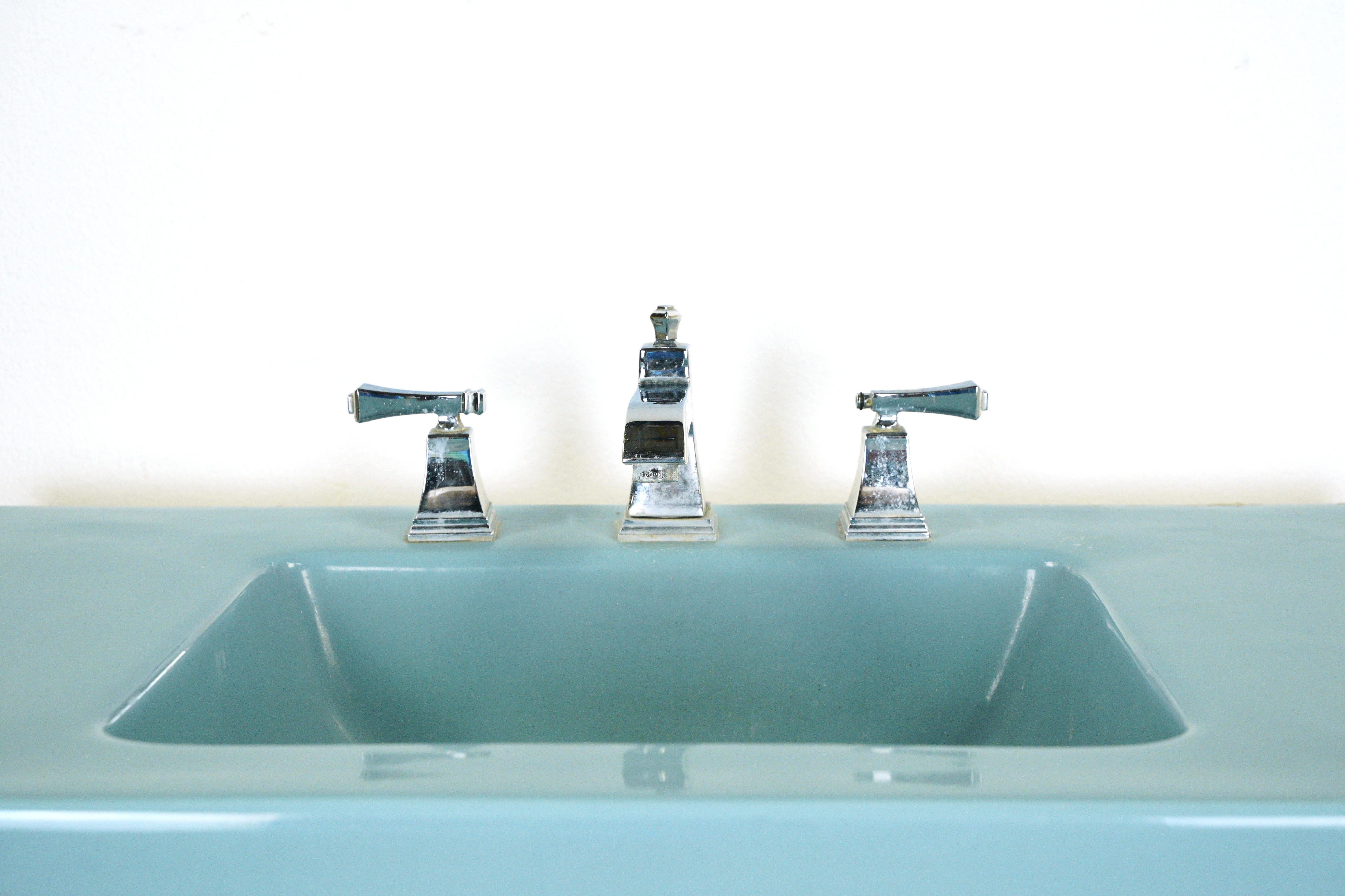 Lavabo de salle de bain sur colonne en céramique bleu sarcelle avec bec et poignées de robinet en acier chromé, deux pieds de support et deux barres porte-serviettes. Fabriqué par American Standard. L'évier est en bon état, avec une usure de surface
