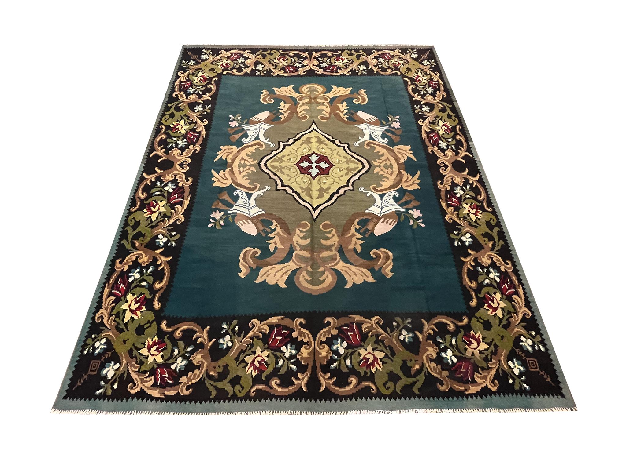 This bold wool kilim is a handwoven masterpiece woven in Moldova circa 1900. The design features a medallion woven on a deep blue-green background in accents of beige, olive green and cream that make up the luxurious patterns. This is then framed by
