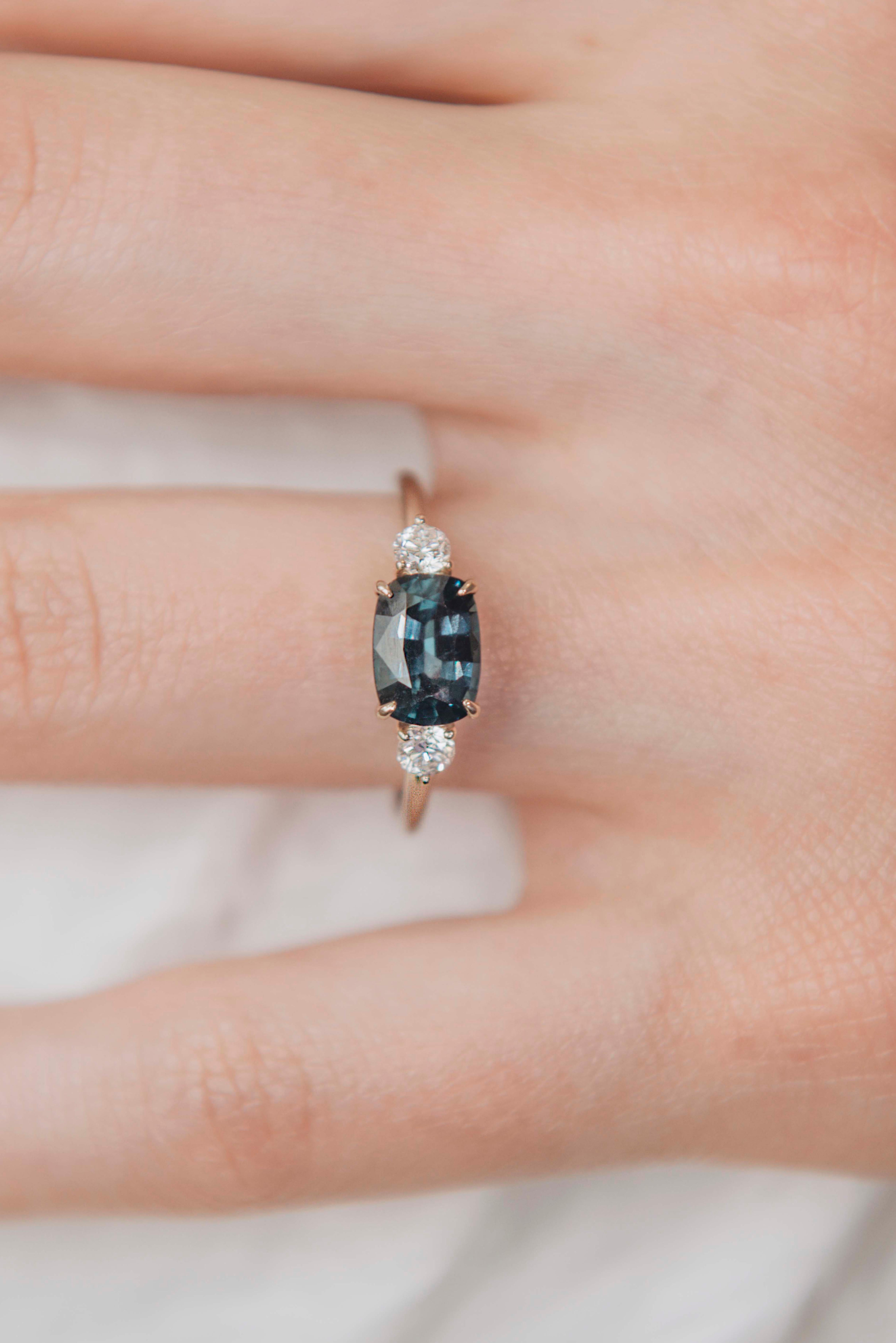 A perfectly made three-stone ring with a well cut no heat 1.33 carat rare teal colored Ceylon spinel flanked by two white diamonds in a comfortable classic low setting in 18k white gold. Pictured without plating with its natural subtle yellowish