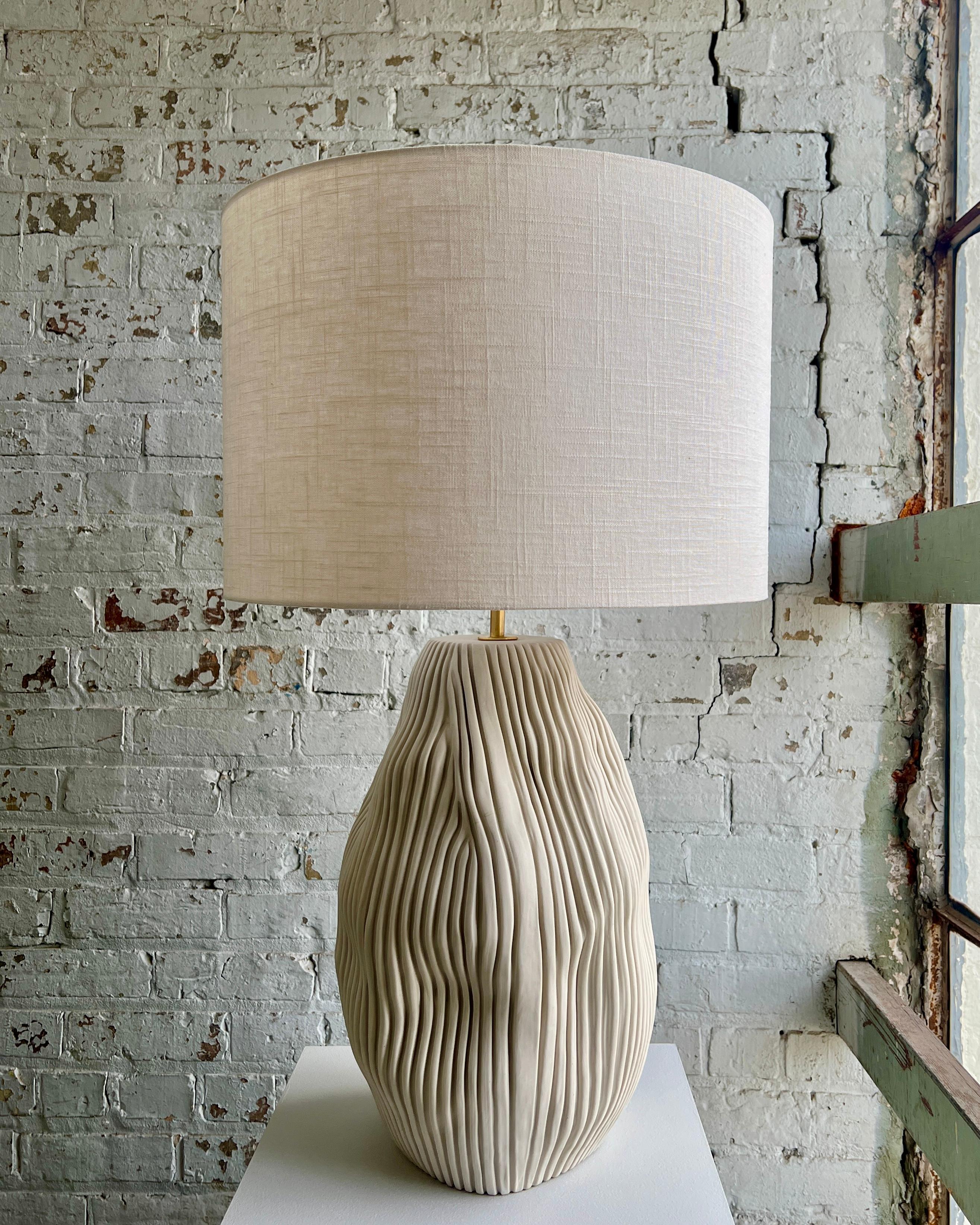 Unglazed porcelain exterior. 6’ cloth covered cord. Solid brass hardware w/ LED dimmer on socket. Off-white linen shade included.
Base Dimensions: 17” High x 10” Wide
Shade Dimensions: 12” High x 18” Wide 
Neck: 2”
Total Height: 31”
Assembled using