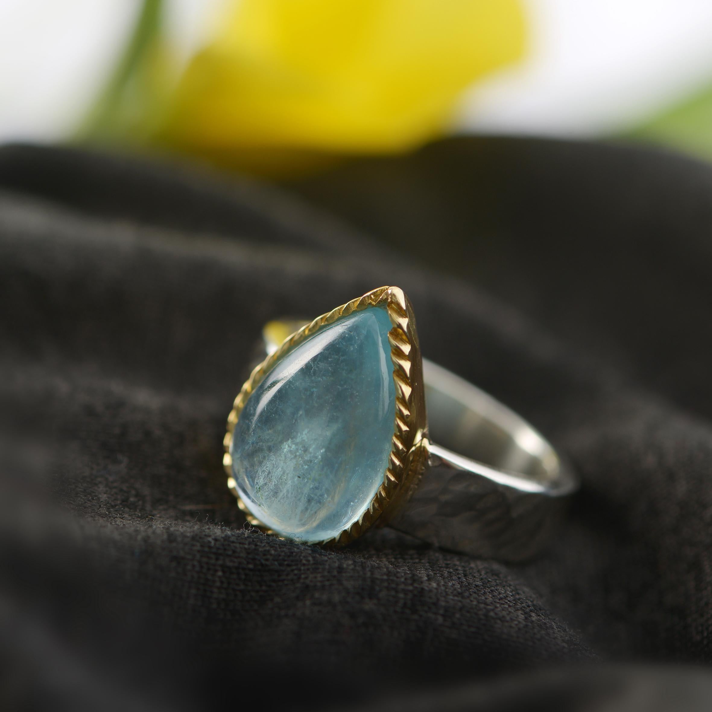 Une magnifique bague en forme de goutte d'aigue-marine cabochon en édition limitée. Fabriqué à la main dans nos ateliers, il présente un cabochon central d'aigue-marine serti dans une plaque d'or 24ct. La tige martelée est en argent sterling.

Il