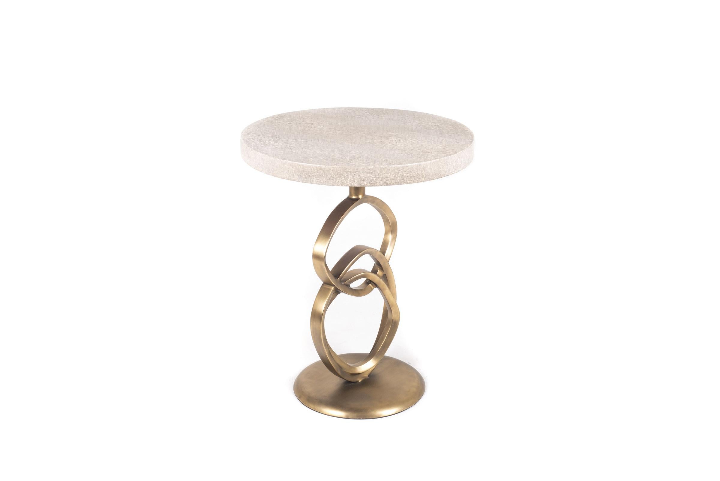 La table d'appoint teardrop I est un design élégant avec des détails exquis. Les anneaux sculptés sont incrustés en laiton bronze-patiné et le dessus est en galuchat crème. Cette pièce est conçue par la fille de Ria & Yiouri Augousti.

La finition