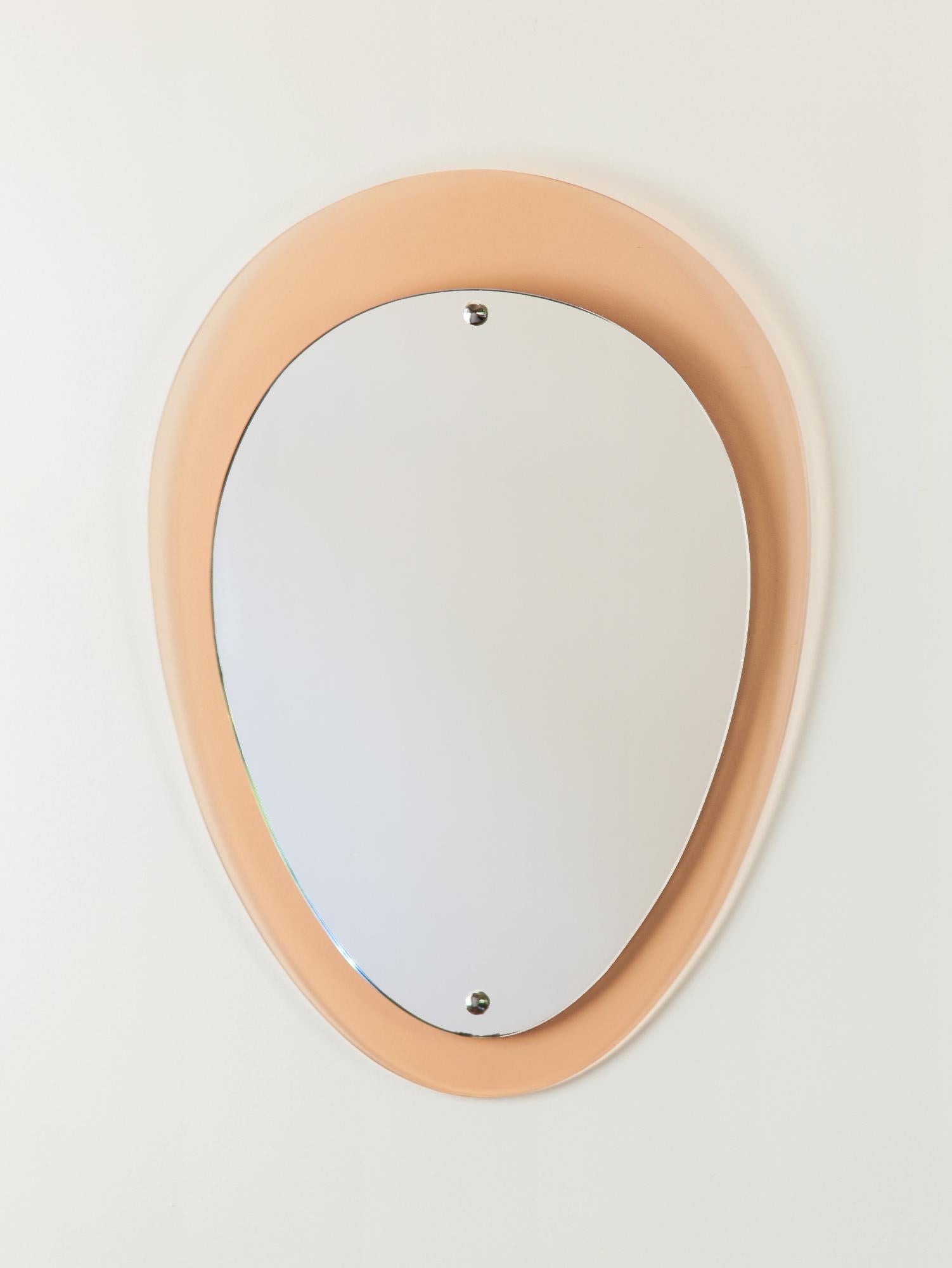 Lovely vintage rose colored glass mirror by Cristal Arte (attributed). The classic teardrop shape glass, with its peachy rose hue, has a lovely beveled edge. The mirror and glass are held by a steel frame on a wooden board with chrome capped screws.