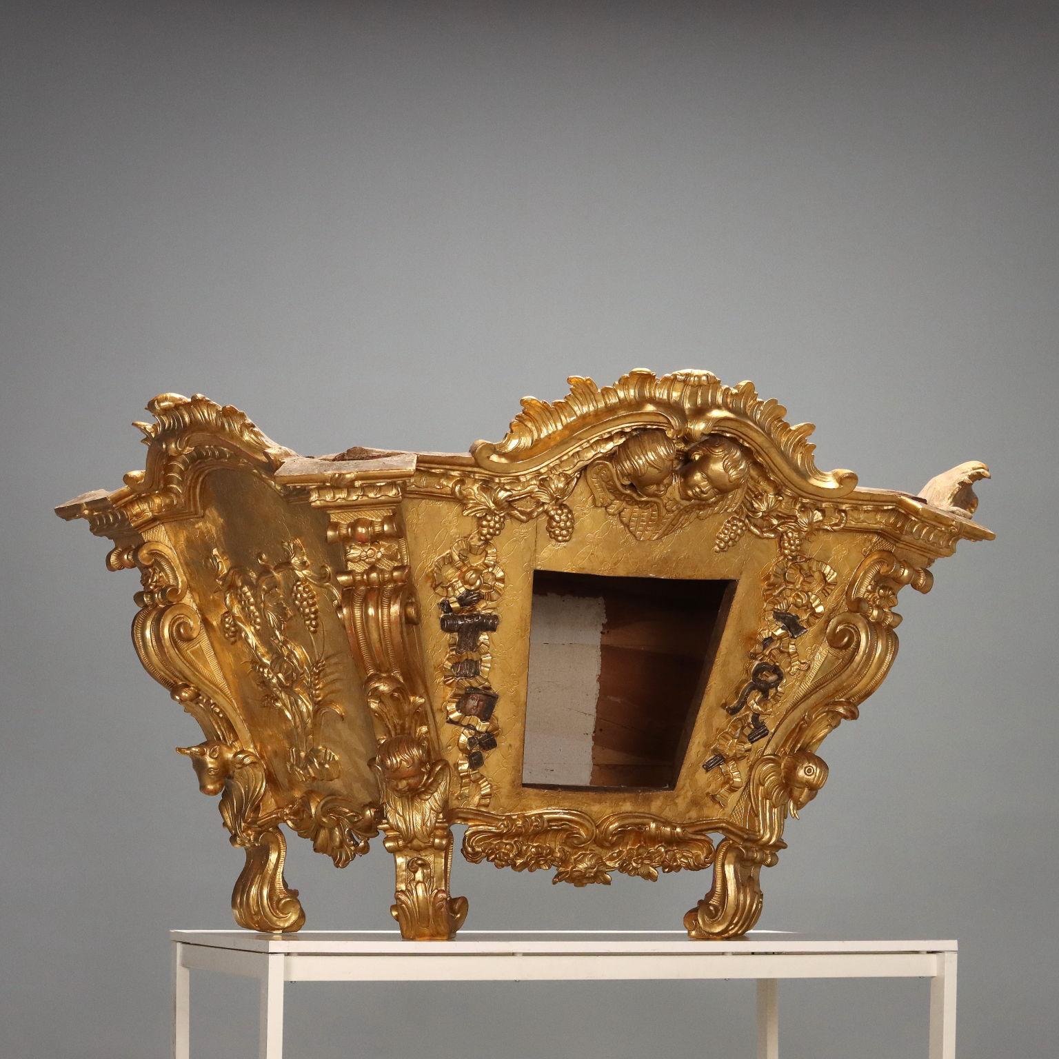 Coffret en bois de tilleul sculpté et doré. Structure pyramidale tronquée inversée à section trapézoïdale, reposant sur quatre pieds ondulés sculptés de rinceaux et de feuilles, tout comme les montants. Les panneaux latéraux sont sculptés d'épis de