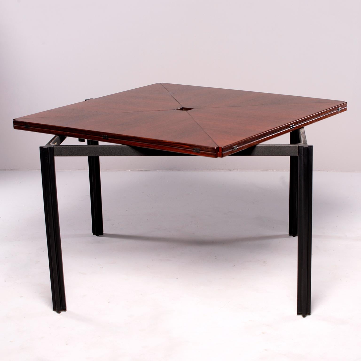 Rosewood table with black metal legs and tagged by Italian furniture maker Tecno, circa 1960s. Square top game table has unique hinged fold up leaves which are accessed by swiveling the tabletop which depresses the nickel button at center, allowing