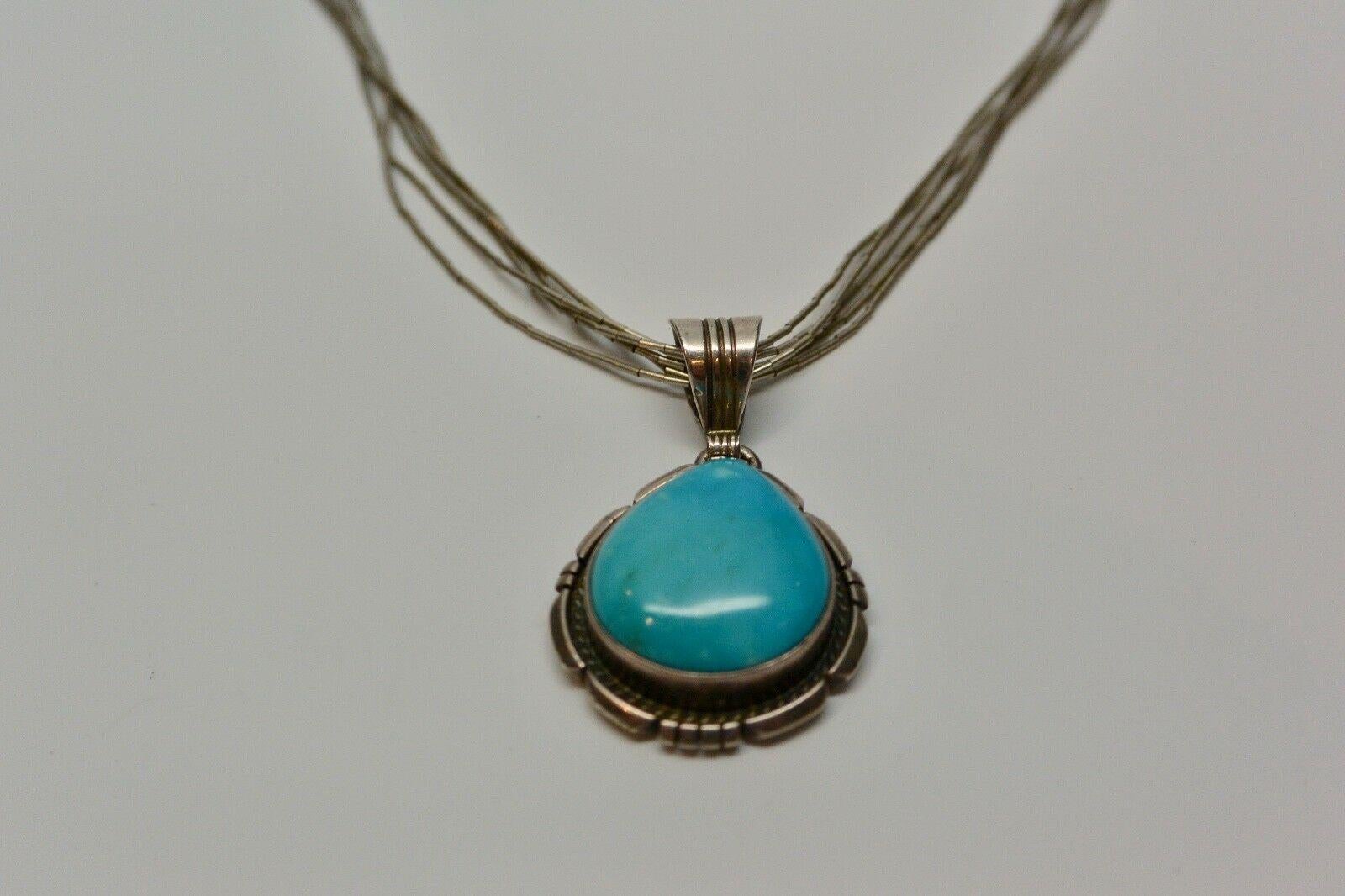 Ted Etsitty Navajo Turquoise Pendant On Liquid Silver Multi-Strand Necklace.

Marked: Sterling

Signed: TE

Measurements:

Strand: 17.25 in long

Pendant with bale: 39 mm x 23 mm

Pendant: 26 mm x 23 mm

Stone: 20 mm x 18 mm, sits 8 mm high

Clasp: