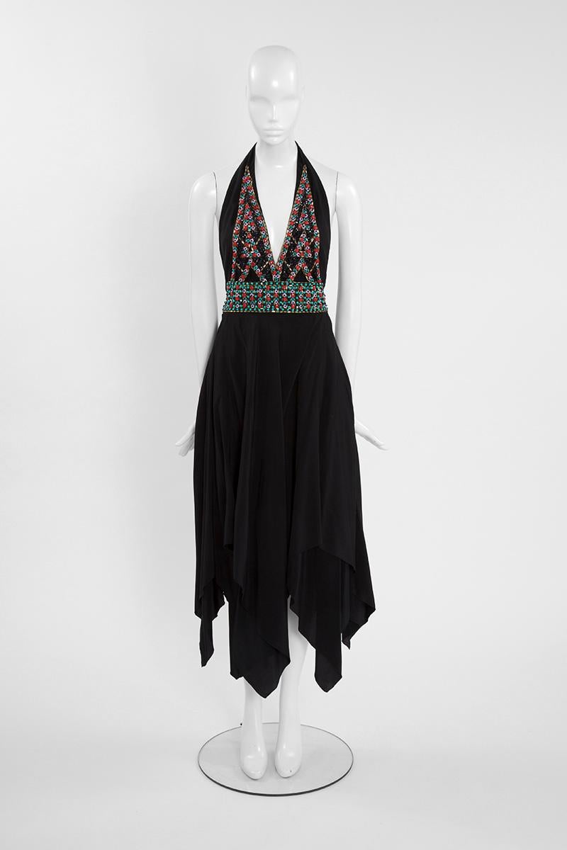 Lassen Sie sich mit diesem Haute-Couture-Abendkleid von Ted Lapidus in die 70er Jahre zurückversetzen! Dieses mittellange Kleid aus schwarzer Seide hat einen glamourösen, tief ausgeschnittenen Neckholder-Ausschnitt, der kunstvoll mit einem bunten
