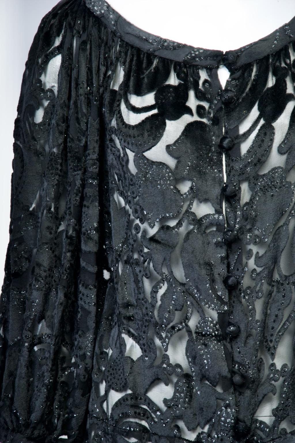 C. Ted Lapidus Kleid aus den 1960er Jahren aus schwarzem Devoré-Samt auf Chiffon-Grund. Der Samt mit Blumenmuster ist mit schwarzen Glitzern verziert, die das Licht einfangen. Das Kleid hat einen Rundhalsausschnitt und runde Knöpfe auf der