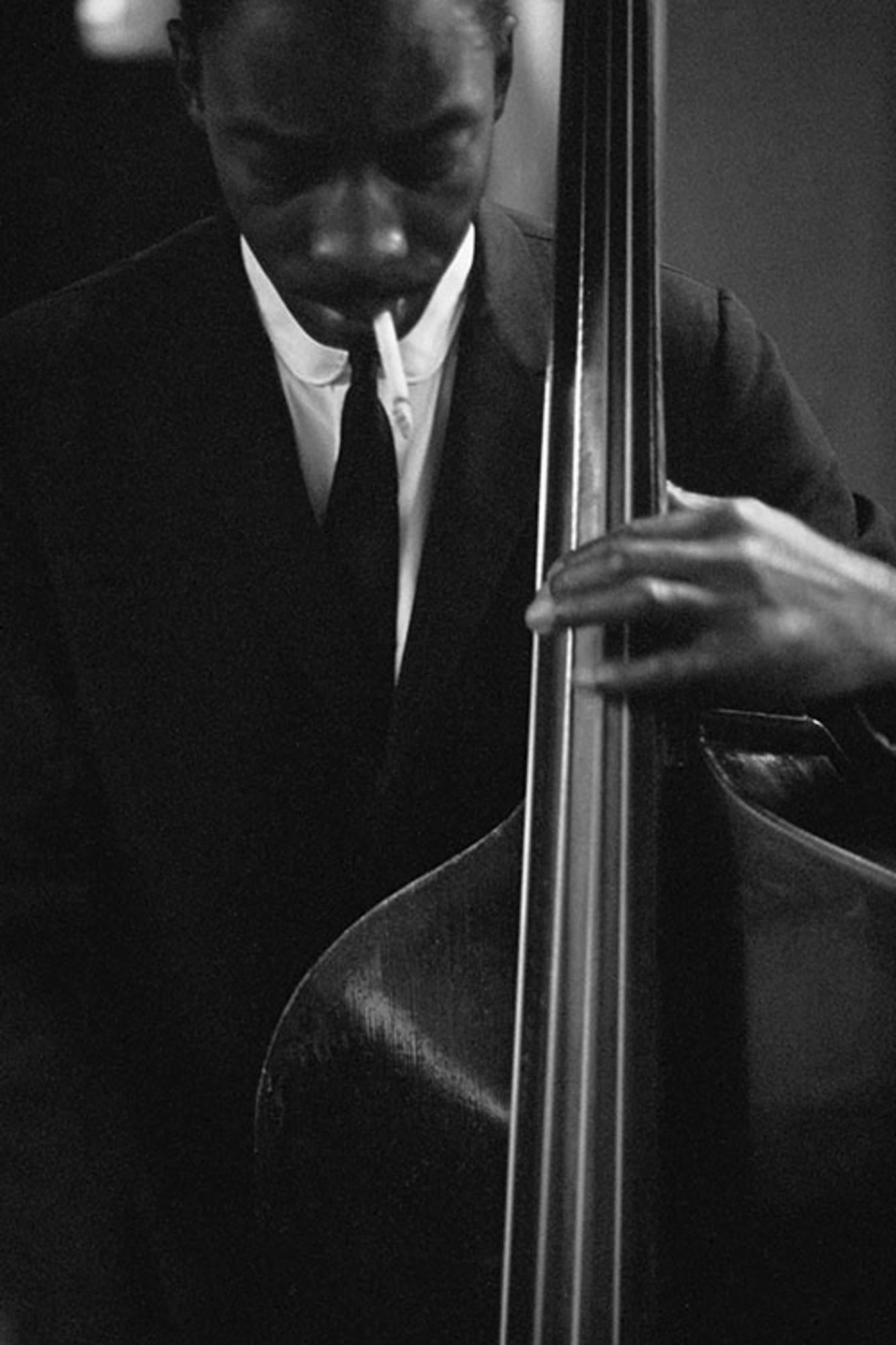Title: Sam Jones Playing the Double Bass Smoking a Cigarette

Estate-stamped, gelatin-print silver

Close-up of jazz double bassist, cellist and composer, Sam Jones playing the double bass whilst smoking a cigarette.

Available sizes: 
20”x16"
