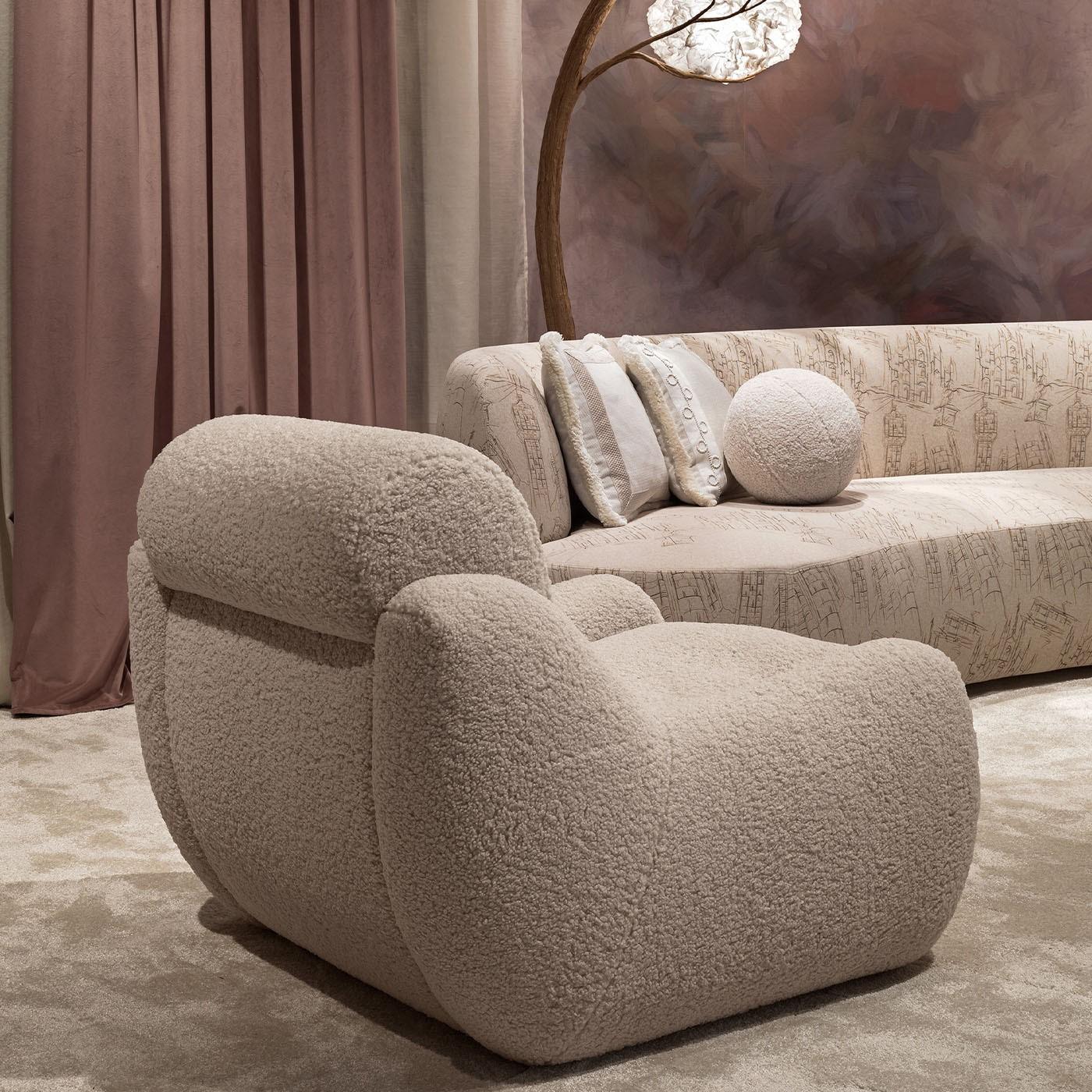 An invitation to enjoy moments of pure comfort between its generous volumes, this enveloping armchair will make for the ideal complement flanking a lamp and creating a cozy nook to relax in the company of a good book. Beige boucle fabric envelops