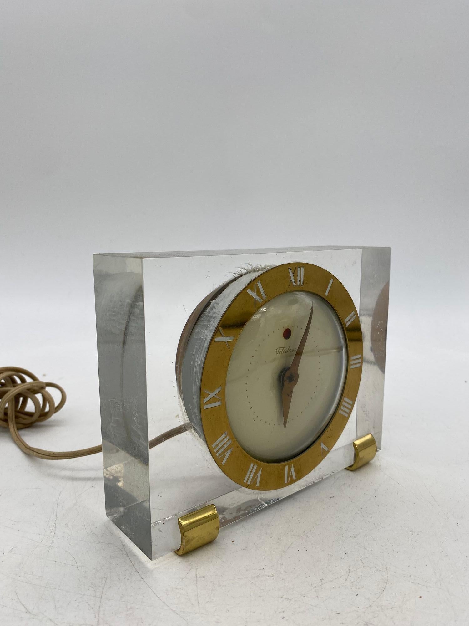 Rare Lucite and brass Telechron Model 7H141 Electric desk clock featuring a brass face with a bubble glass front fitted inside a highly polished square acrylic block with brass feet.

Measures 5 1/2 inches tall
7 1/2 inches across
2 1/4 inches