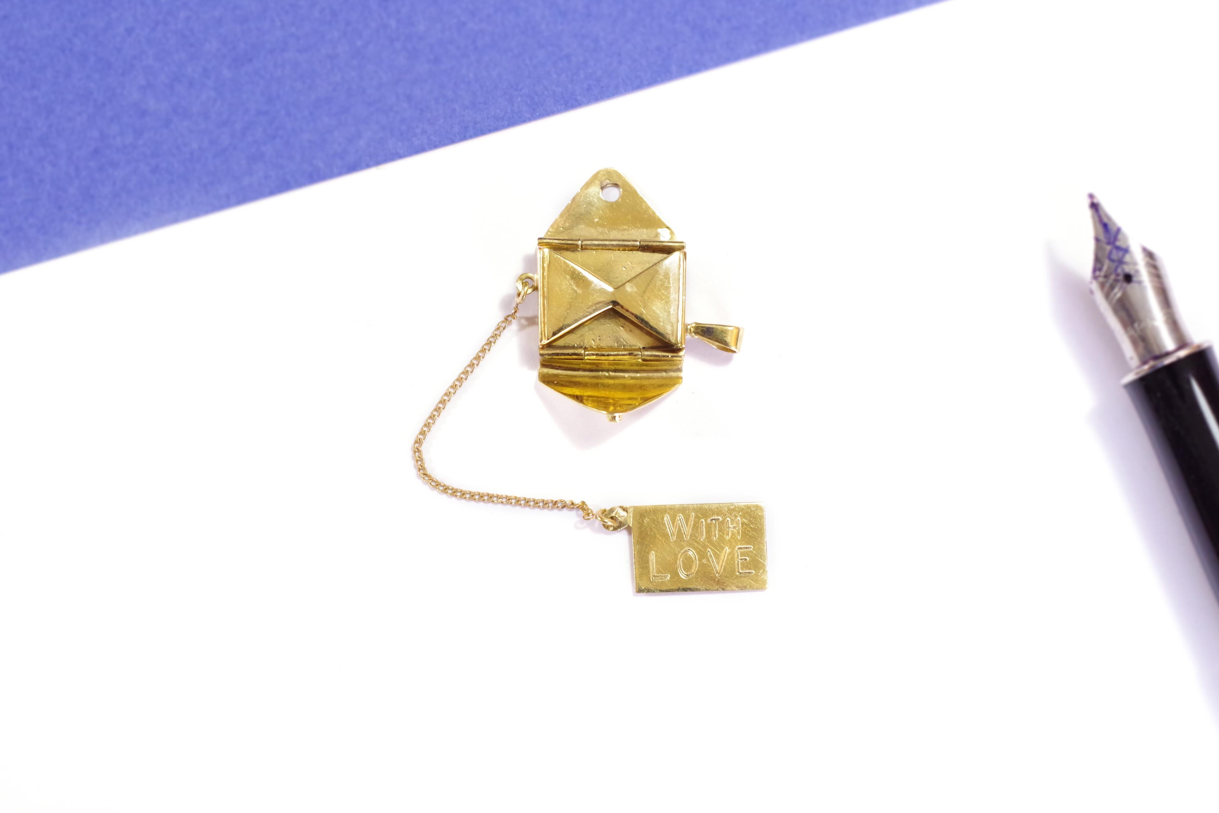 Telegram love letter pendant in 18 karat yellow gold. Pendant charm taking the shape of an envelope, set with a square cut sapphire symbolizing a stamp. It is a jewel with a secret: the envelope opens on a love letter, which is mobile. The