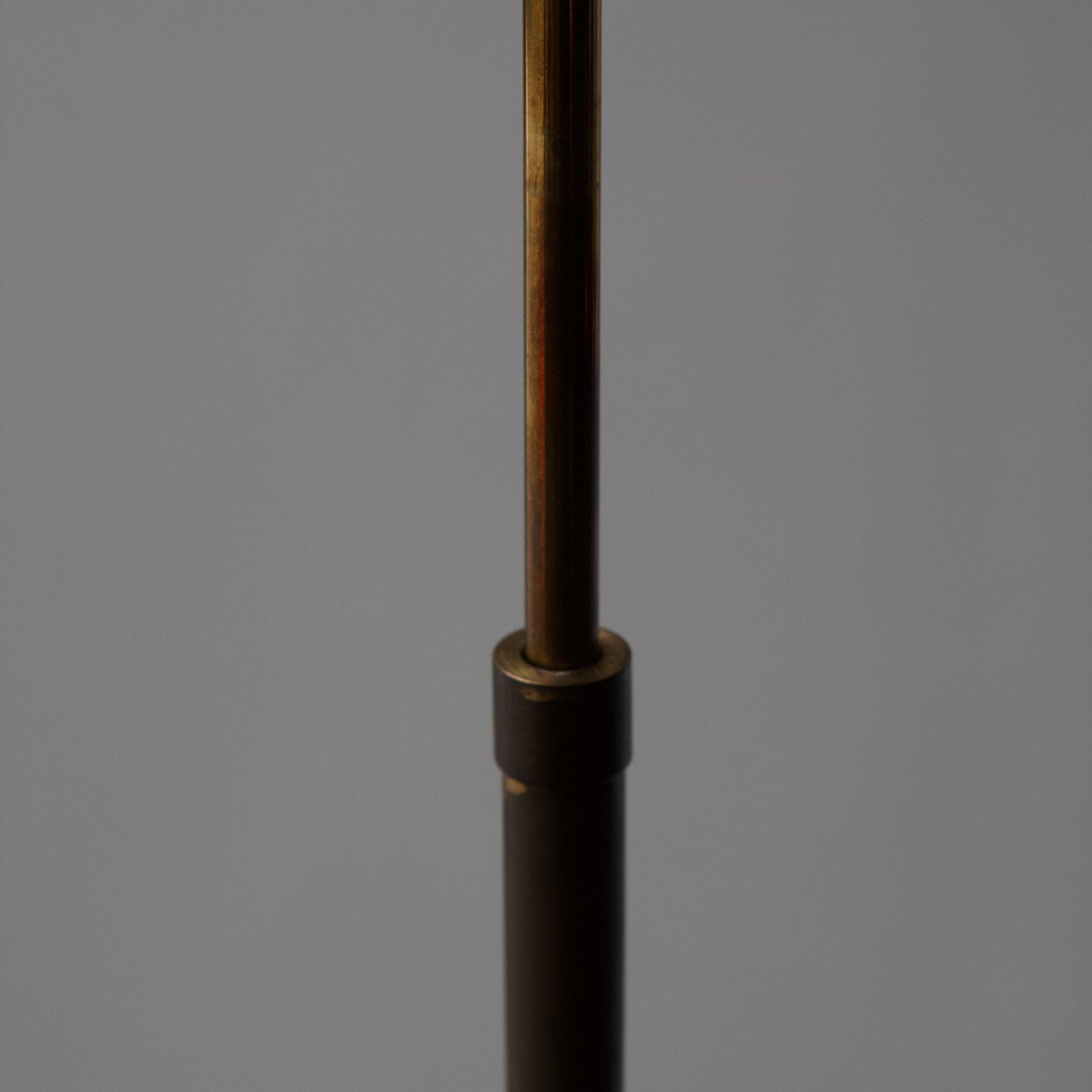 A slim brass floor light with telescopic extension, allowing the height to be lowered or raised. 

The base, stem and distinctive curved bulb holder of this lamp are richly patinated. The brass appears lighter at the centre as a result of the