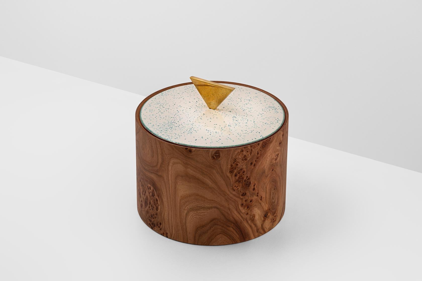 Joyero cilíndrico de madera de olmo tratada con aceite de bergamota. El tapón, cóncavo por un lado y convexo por el otro, es de cobre esmaltado. Es abatible y se puede utilizar por ambos lados, uno caracterizado por un pomo triangular y el otro por