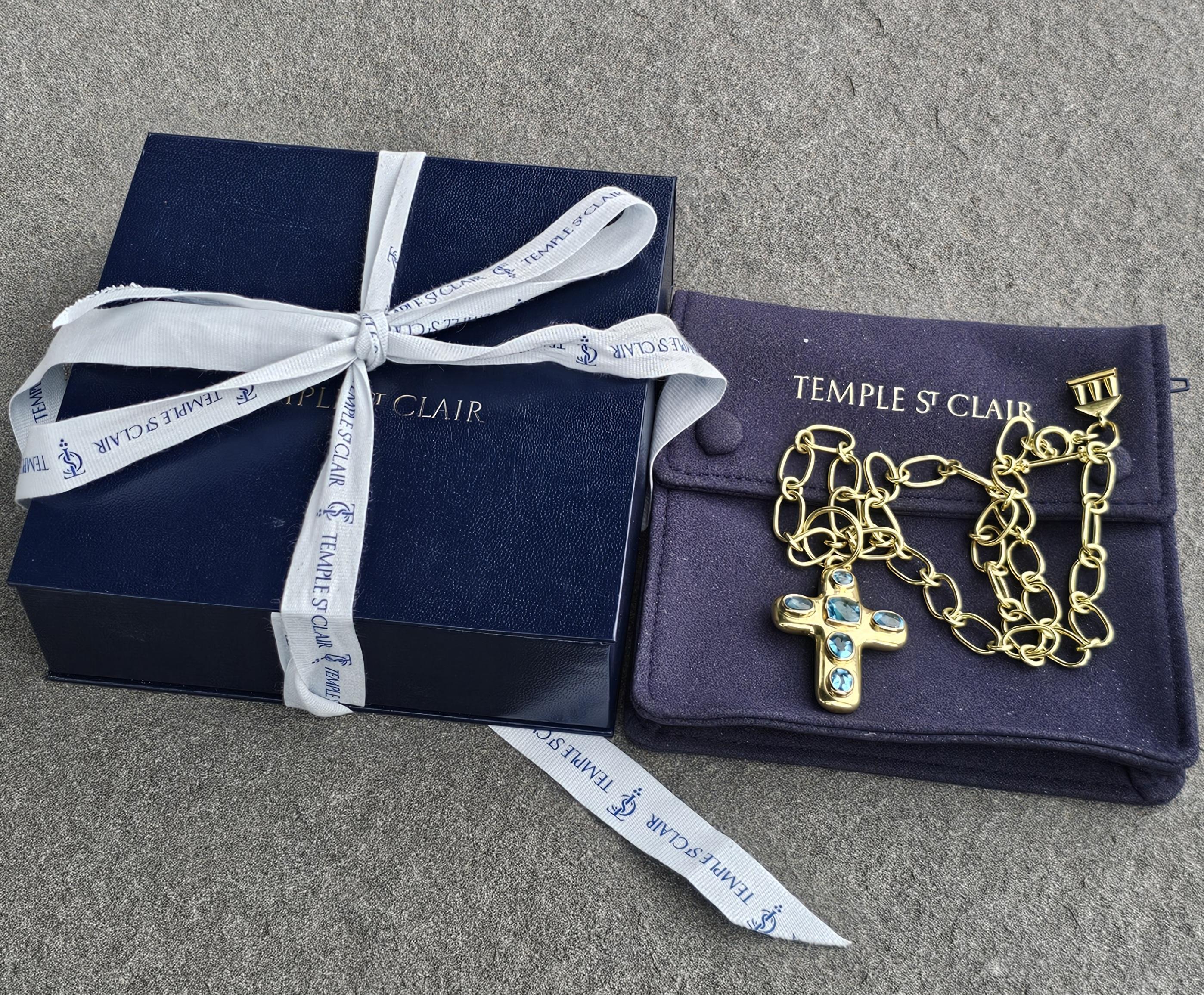 This Temple St. Clair pendant necklace is a captivating piece of fine jewelry featuring vibrant blue topaz stones set in 18k gold. The cross-shaped pendant is adorned with multiple blue topaz stones, creating a striking and elegant design. The