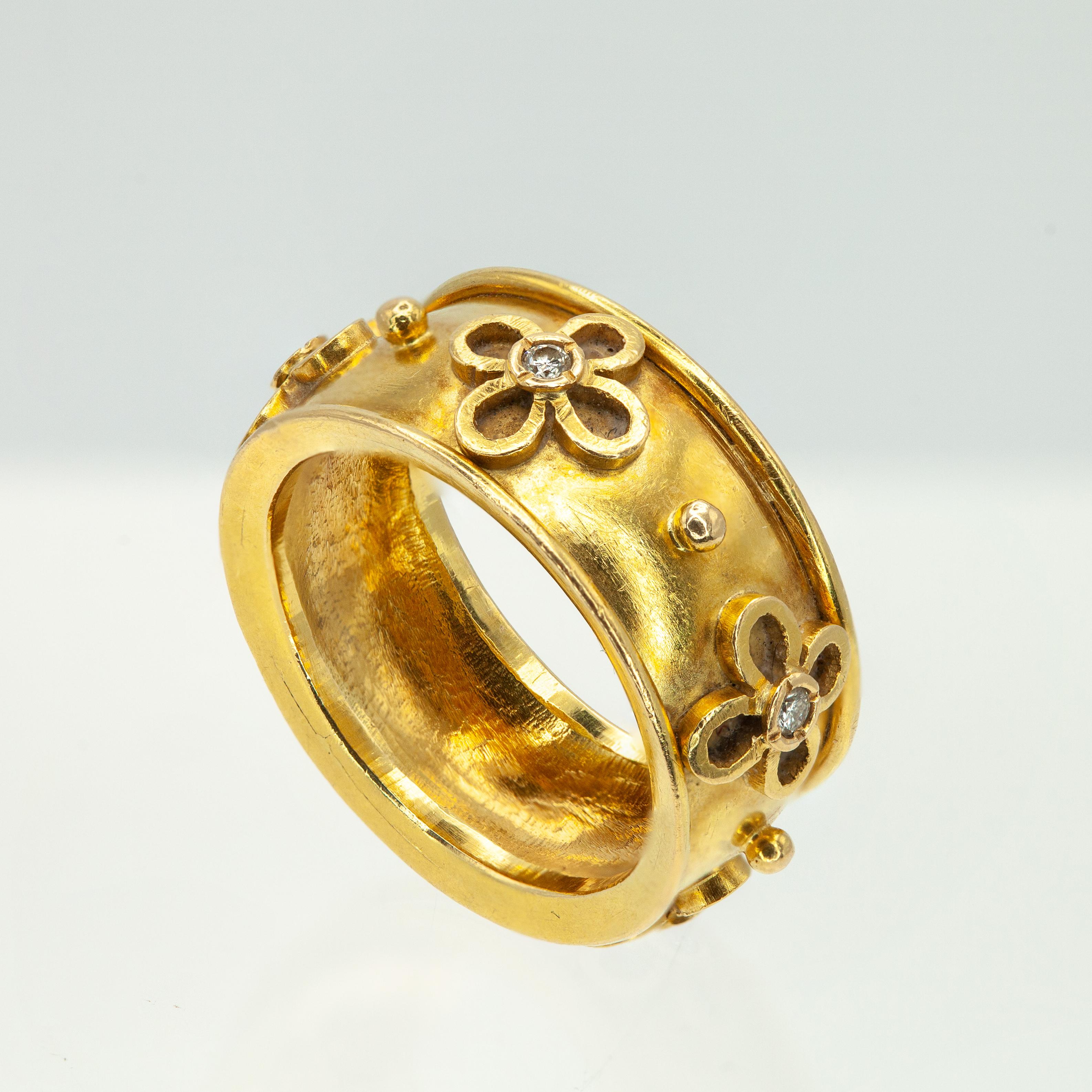 Questo elegante anello a fascia larga di Temple St. Clair è realizzato a mano in ricco oro giallo 18 carati. Il design è caratterizzato da dettagli di granulazione e motivi floreali stilizzati, ognuno dei quali è centrato da un diamante dal taglio