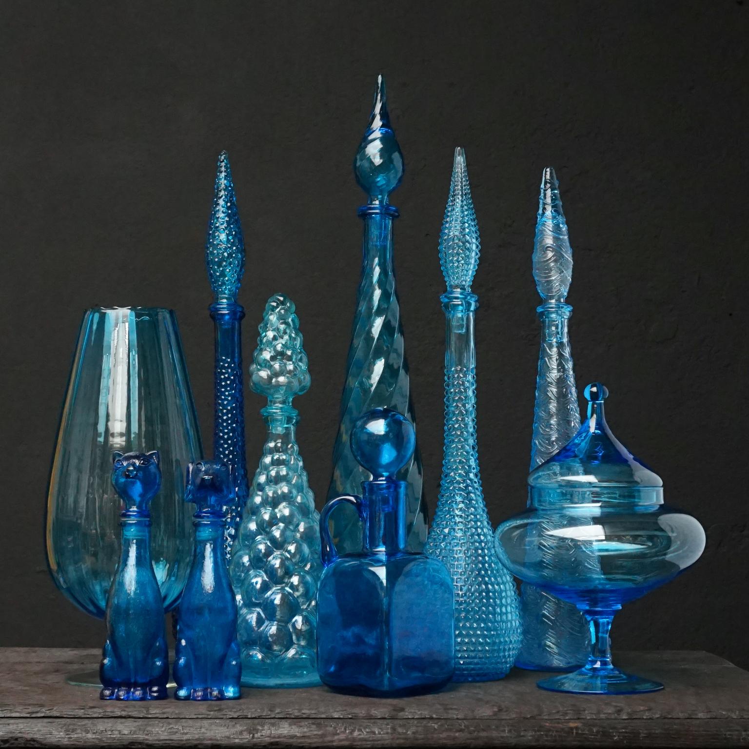 Very decorative blue set of eleven different size Italian blown and pressed glass bottles.
Four genie bottles, a pressed bubble carafe, a square carafe, a blown vase and an apothecary or candy jar and last but certainly not least a little cat and