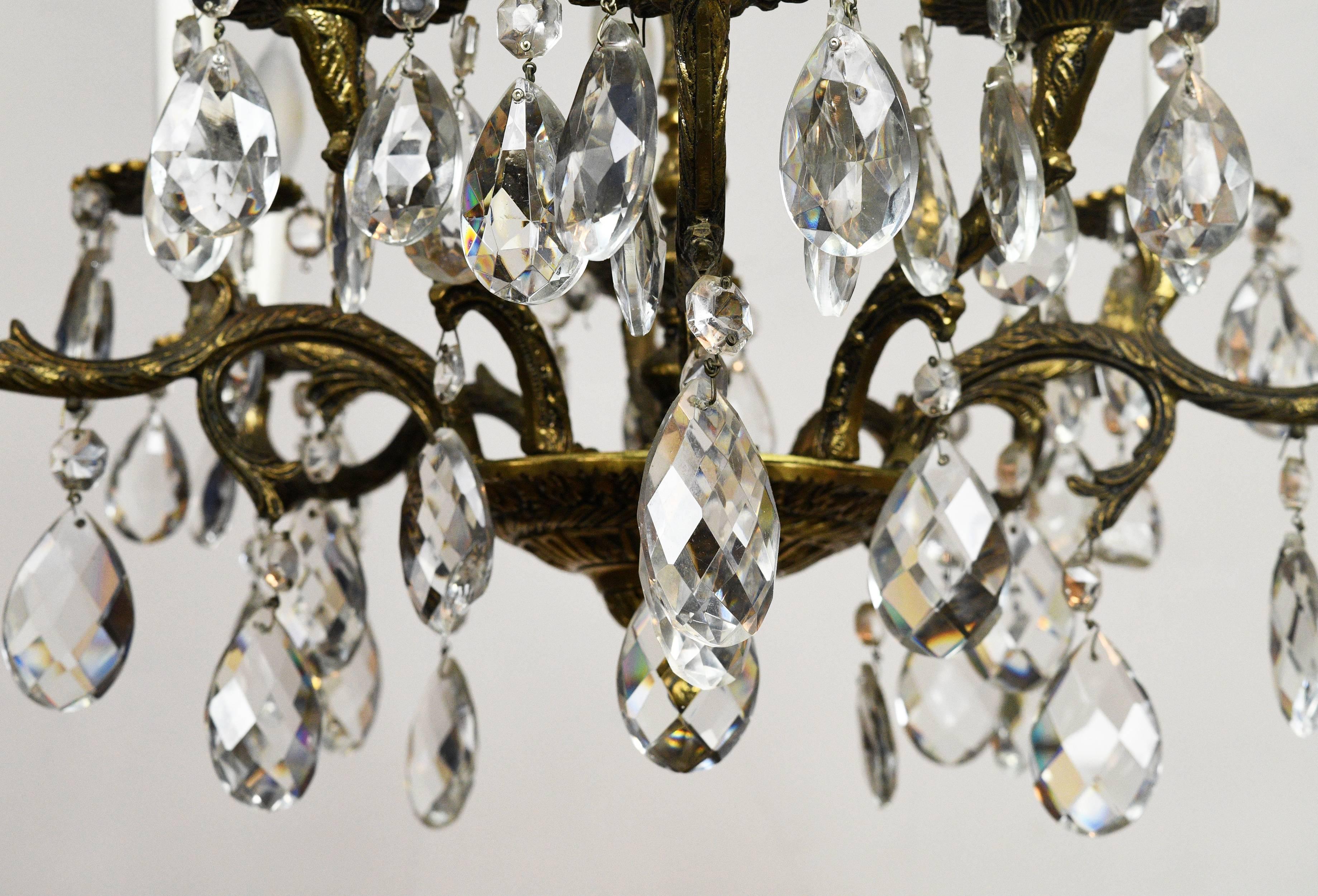 Un lustre espagnol complexe et sophistiqué avec des cristaux:: fabriqué en Espagne. Il comporte dix bras placés à différentes hauteurs. Des motifs de feuilles très détaillés sont gravés sur l'ensemble du corps en laiton. Si vous êtes à la recherche