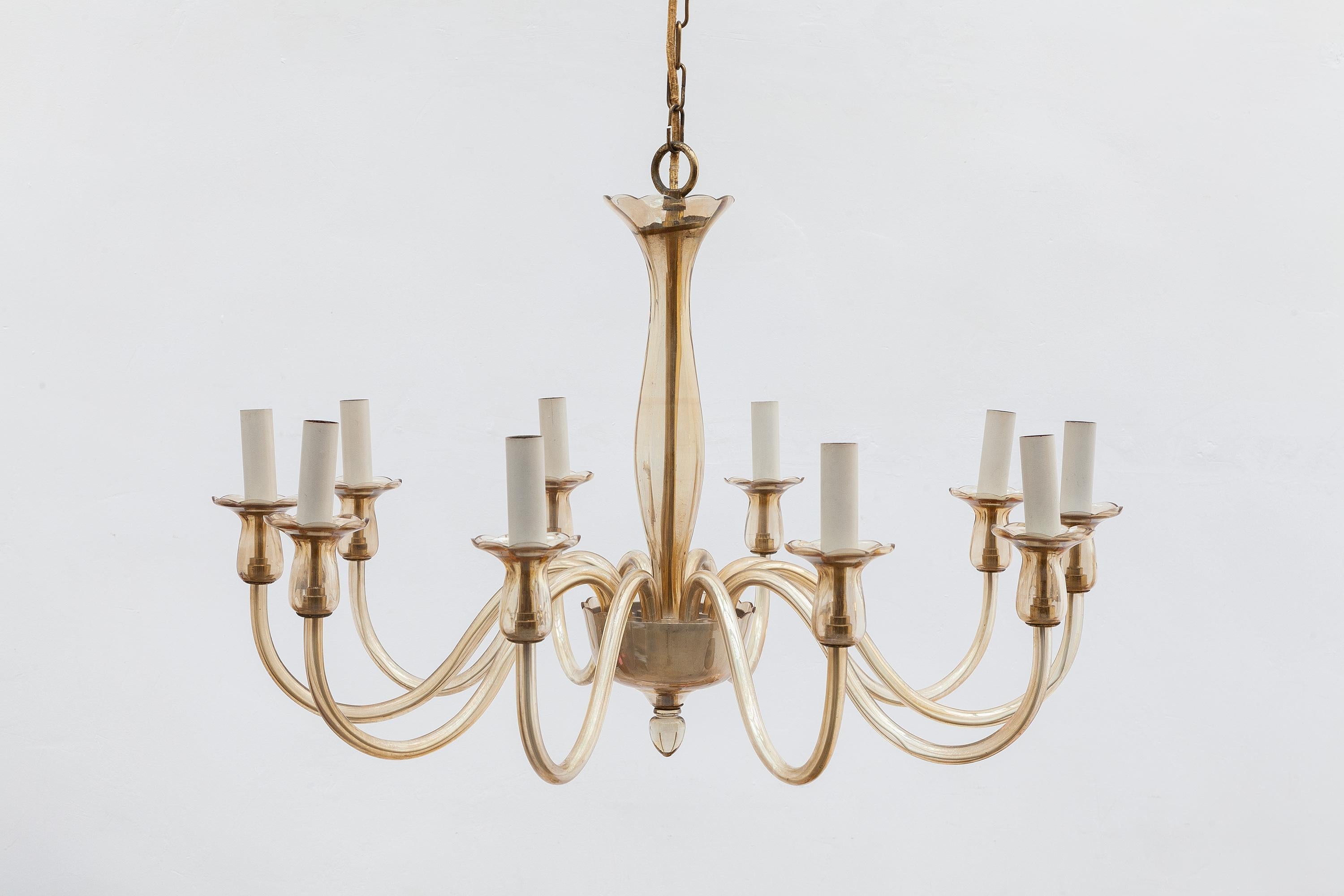 Hollywood regency style chandelier in warm amber colored glass with brass tone hardware. 10 arms with candelabrum sized sockets.
Dimensions: 83 W x 51 H cm, chain length 150 cm.