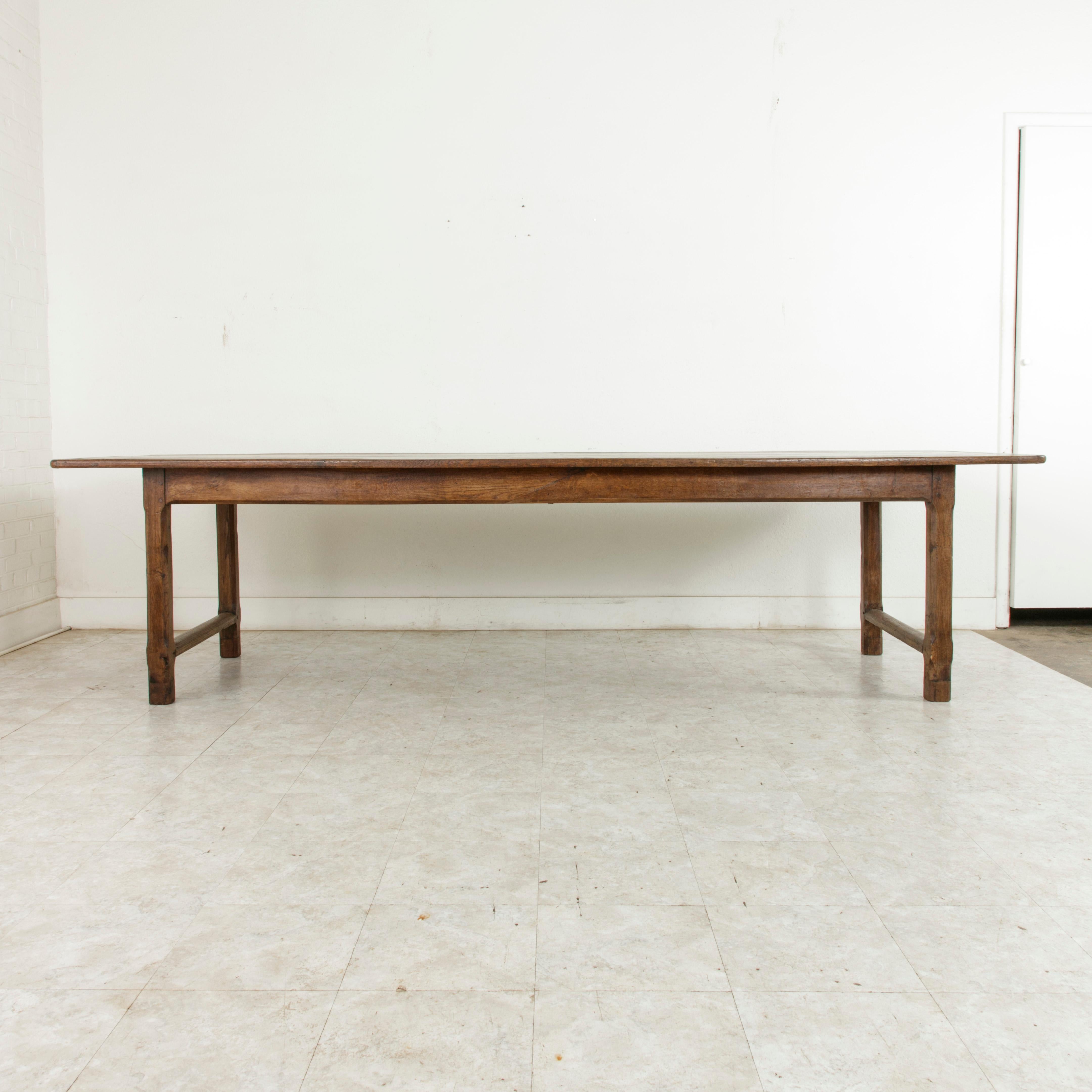 Spanning nearly ten feet in length, this large oak farm table or dining table from Normandy, France, features a 38-inch wide top and a hand pegged base of mortise and tenon joinery. A stretcher spans between the legs at each end of the table,