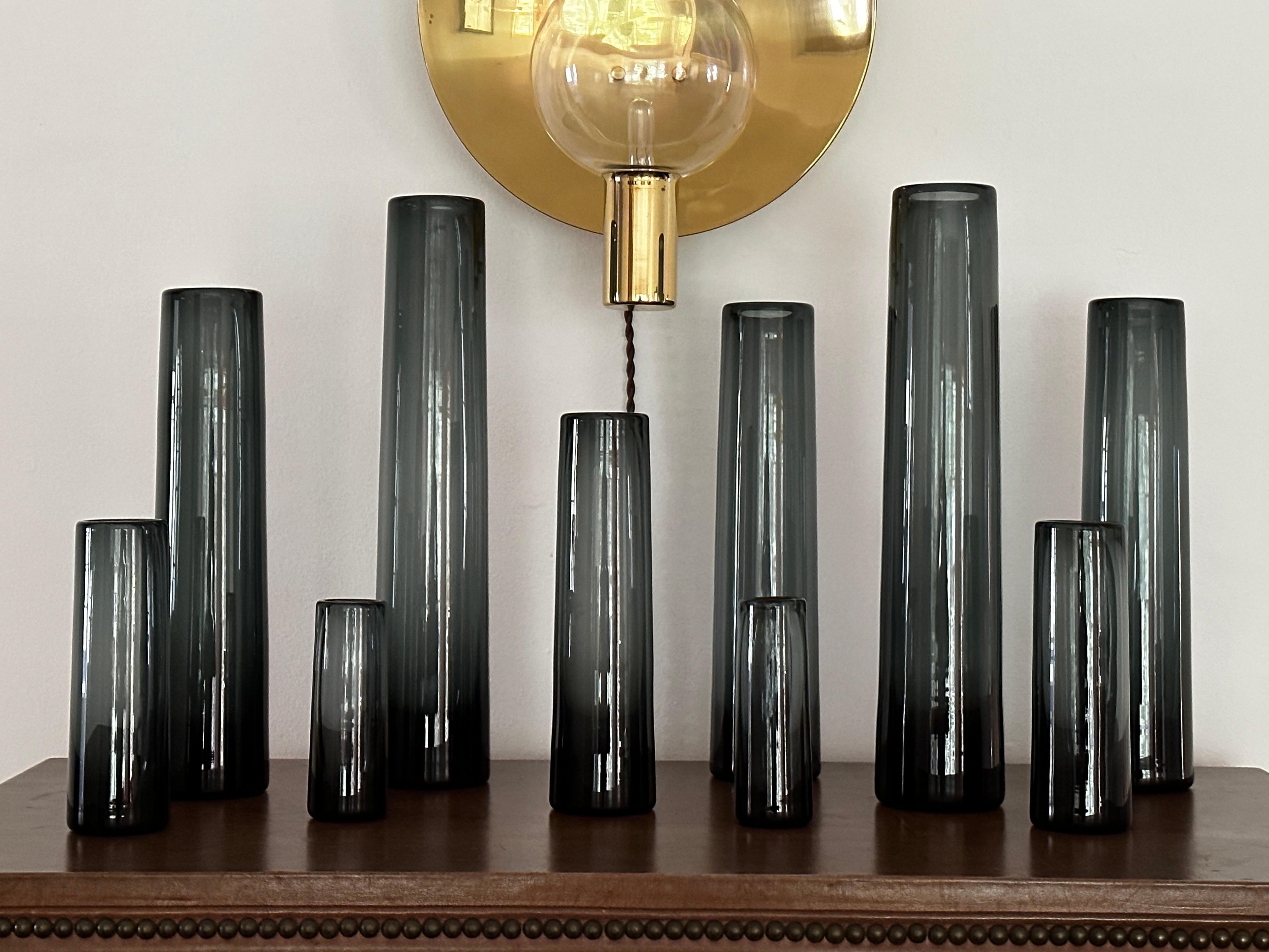 Ten vintage Holmegaard smoke gray, hand blown, cylinder vases designed by Per Lütken.  

Per Lütken (1916–1998) was a Danish glassware designer who studied painting and technical drawing at the School Of Arts And Crafts in Copenhagen.  In 1946