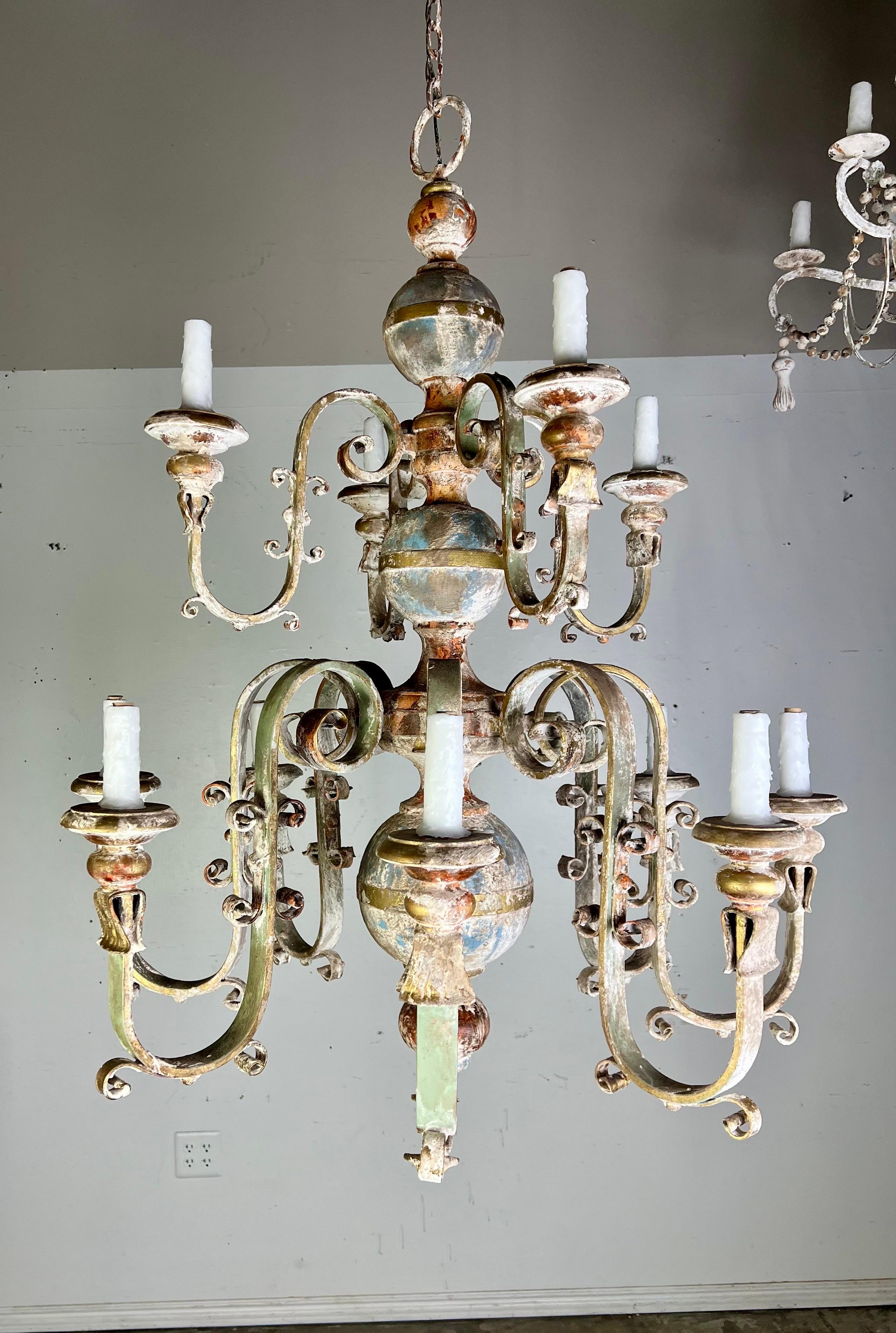 (12) light Spanish Baroque style wrought iron & wood painted chandelier.  This chandelier has a rustic antique design with a distressed patina finish that blends tones of aged god, bronze, grren, blue and hints of white.  The central structure 