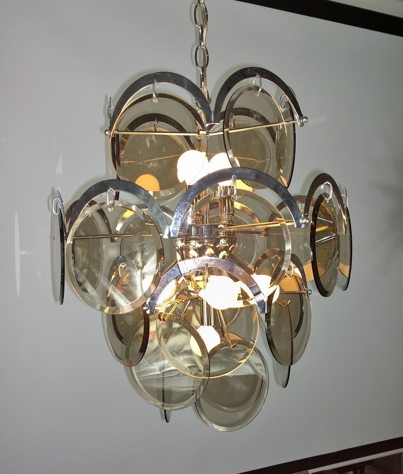 Offered is a Mid-Century Modern Italian Vistosi attributed ten torchère chandelier with four graduated tiers of beveled smoked glass discs framed by half-moon shaped plated chrome and chrome frame. Both elegant and modern, this piece is highly