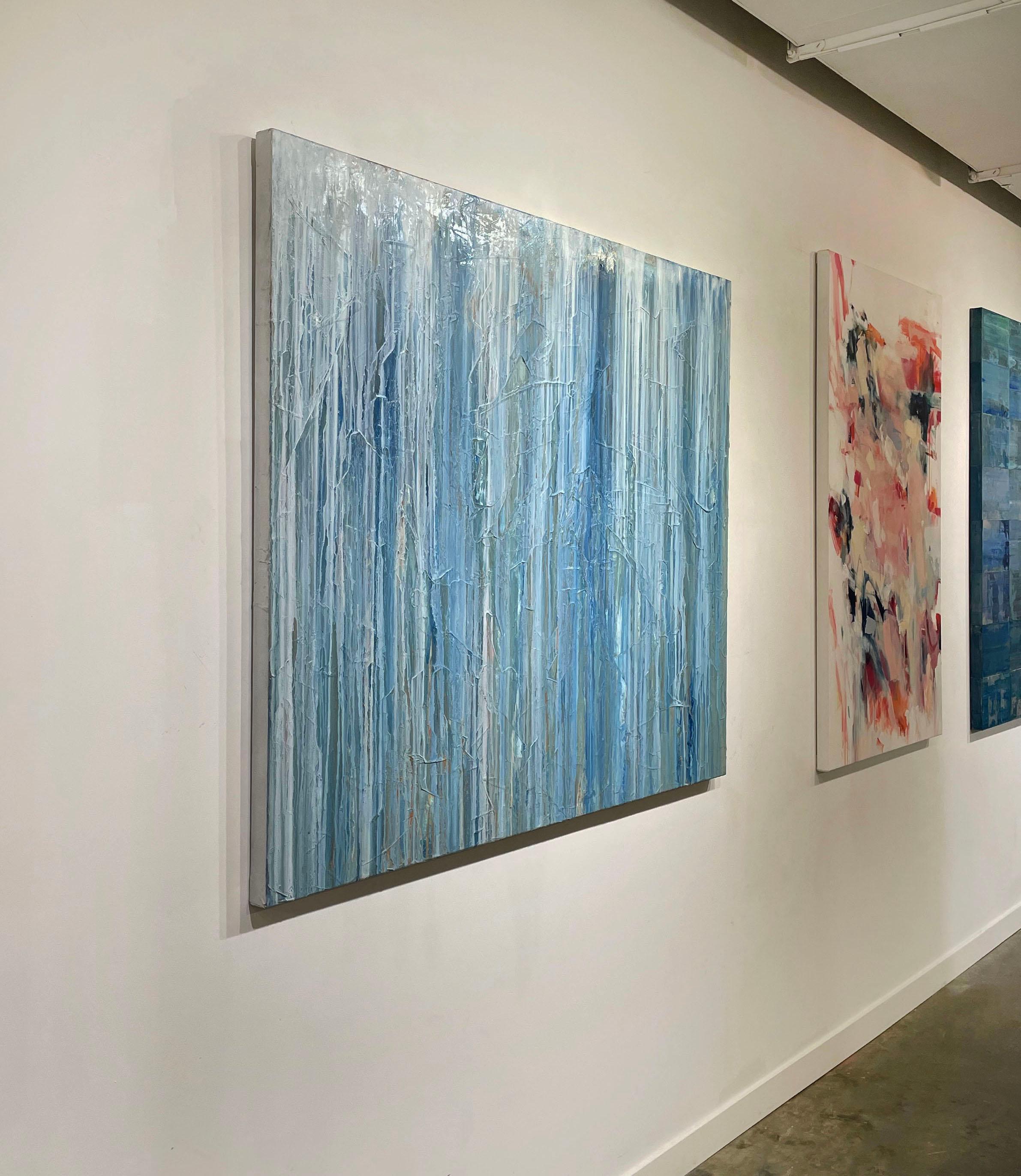 This large abstract statement painting by artist Teodora Guererra is made with oil paint on gallery wrapped canvas, and has clean, platinum painted sides. Blue and white paint appears to fall in light layers of drips down the canvas, over a textured
