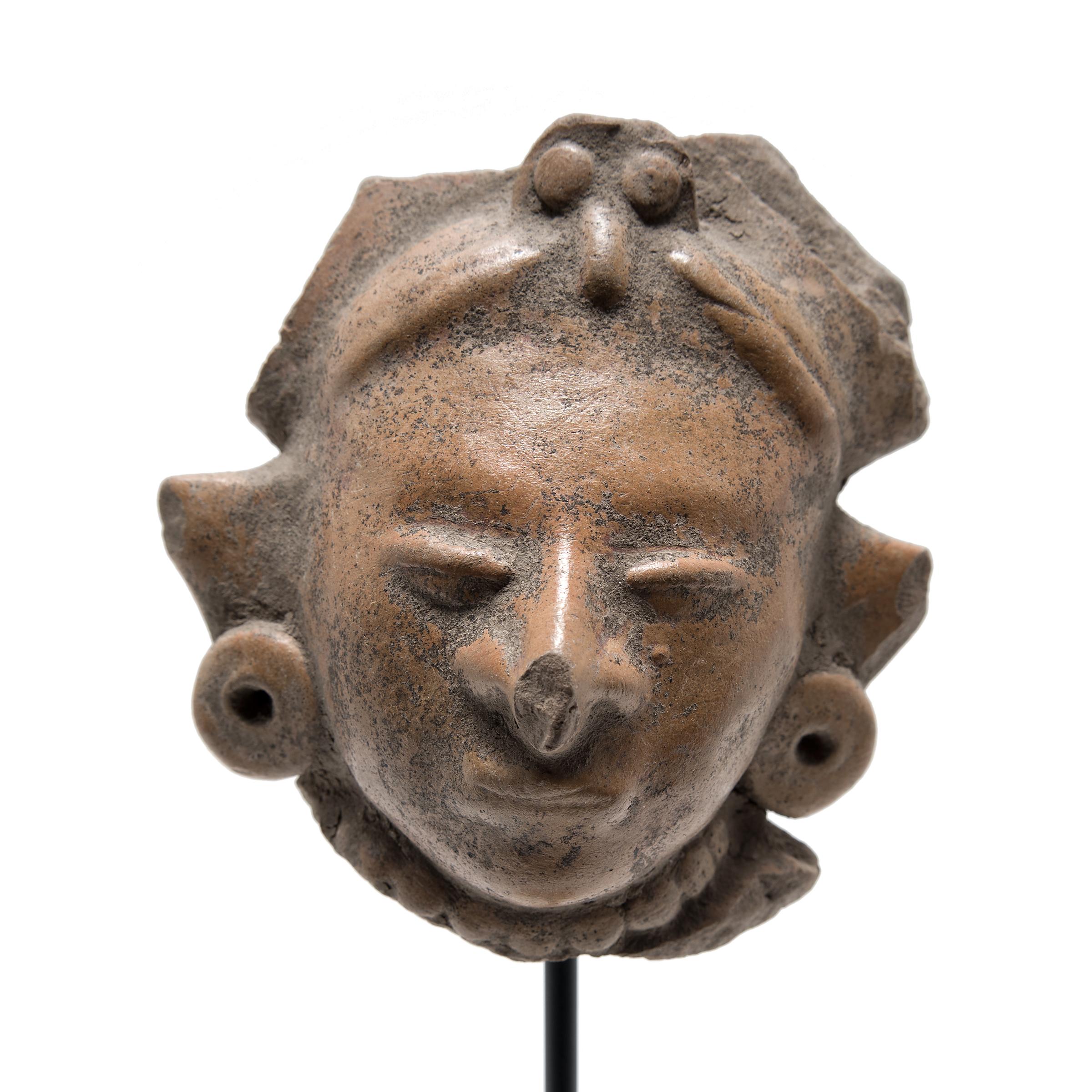This intriguing head fragment was once attached to a bust or full effigy figurine crafted in 400 A.D. Mesoamerica. Earthenware figurines were made in great abundance throughout Teotihuacan's history. After 250 A.D. objects made from clay increased
