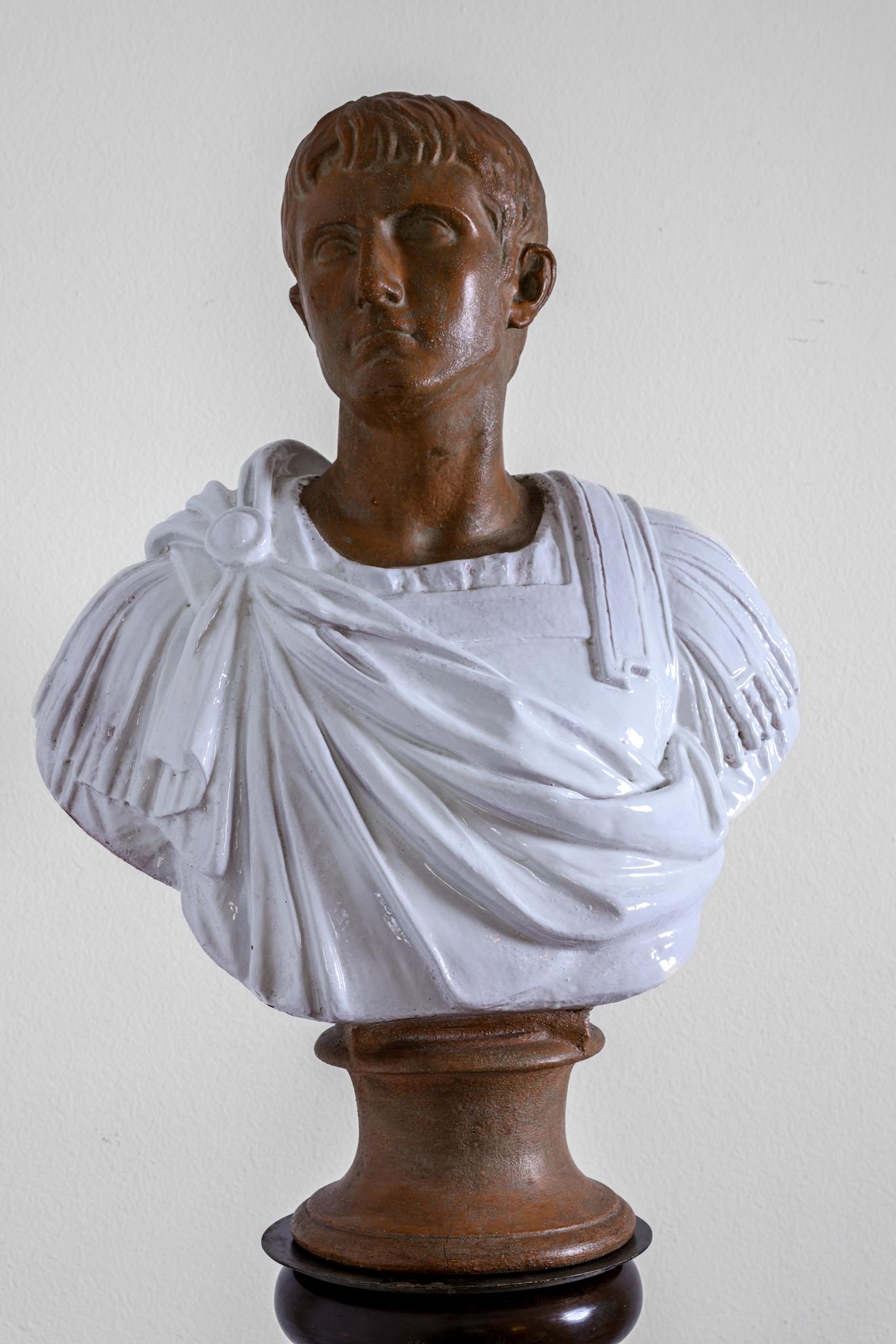 This terracotta sculpture depicts the bust of a Roman Senator or Emperor in armor and a gown. Hi gaze is directed at about a 45 degree angle. This is a magnificently robust life size bust. The garment has been fired in a white glaze. The bust has a