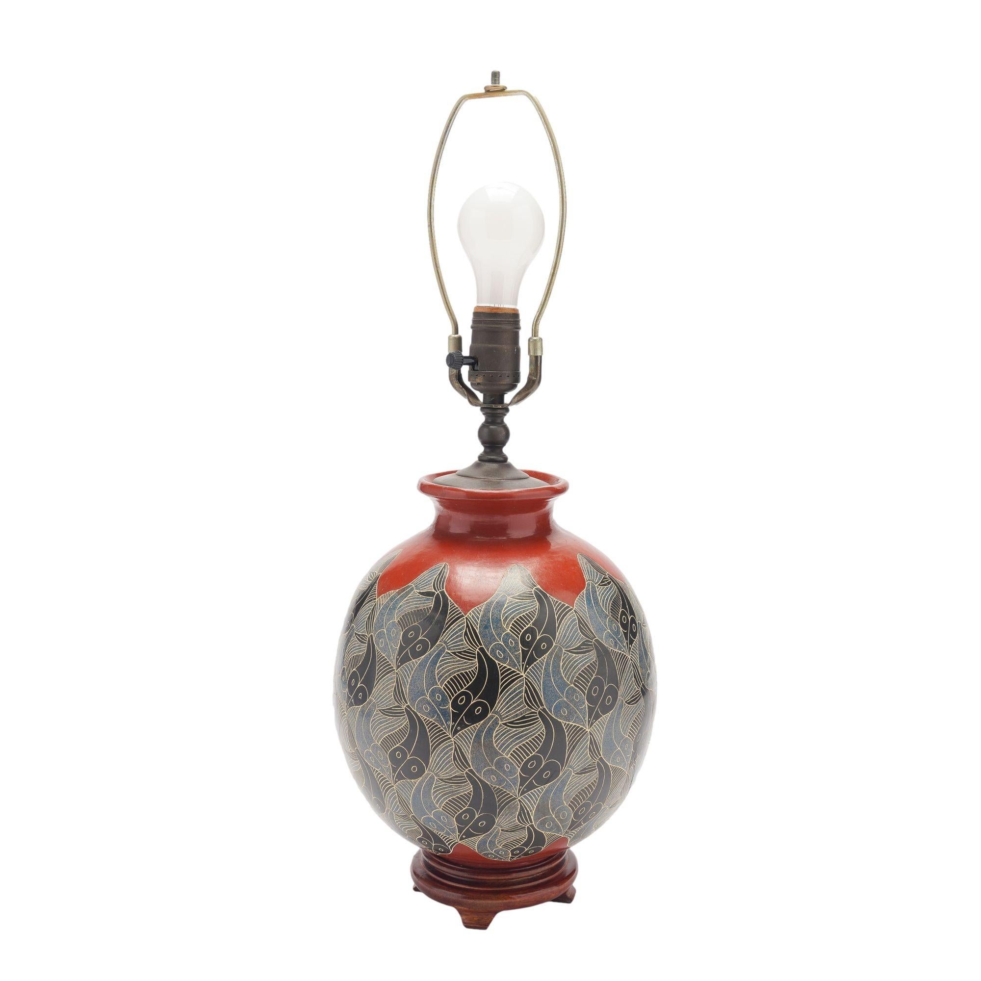 Terra cotta vase decorated with Escher-inspired graphic repeating patterns of fish using traditional clays and incised line decorating techniques with cobalt blue glazes. Wired and mounted on a turned hardwood base. Does not come with shade.

Signed