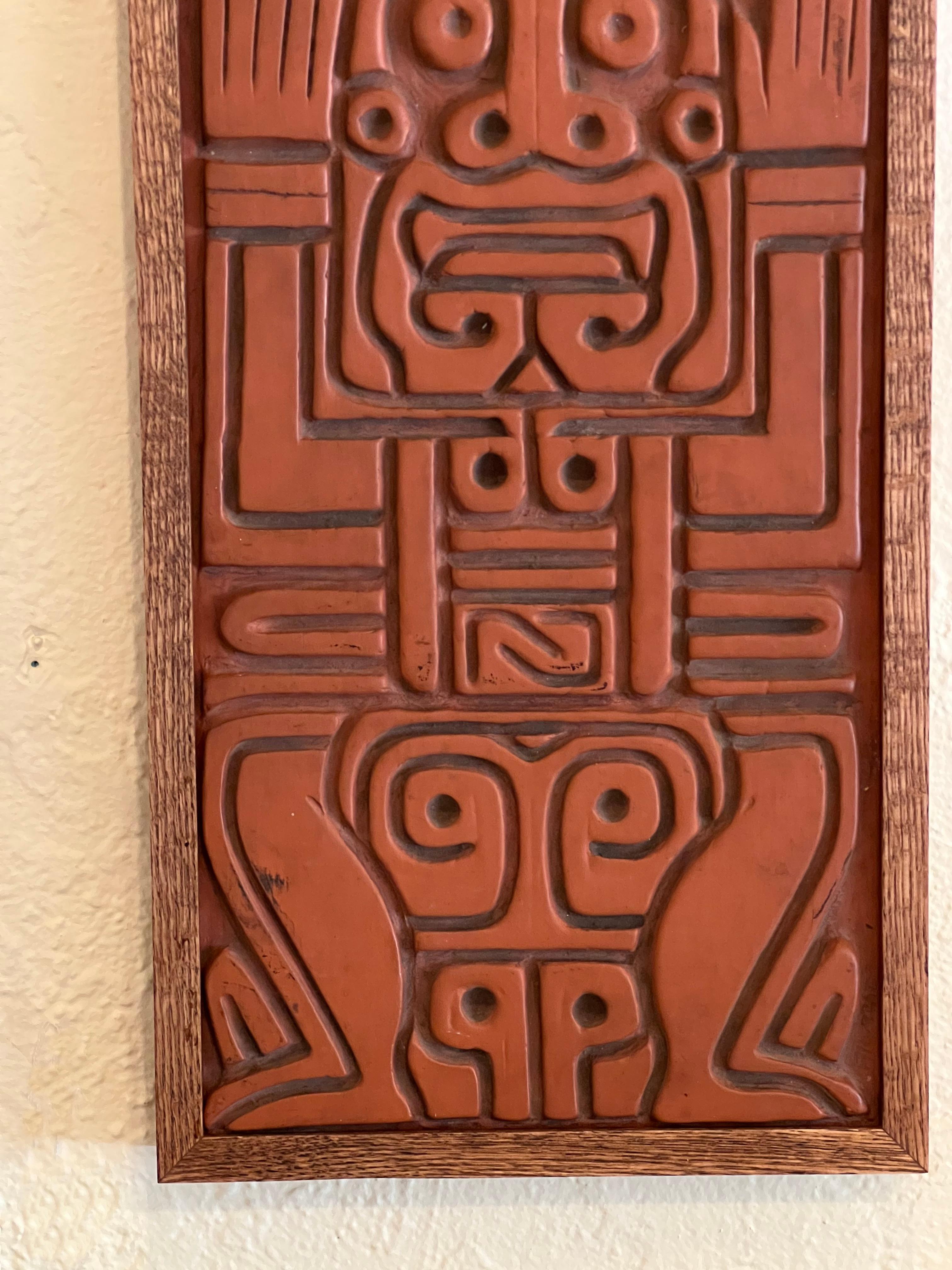 This wall sculpture by Albrecht is a three-dimensional piece with a Mayan design that appeals to the sense of touch. It is made of molded terracotta, hand-finished with a polished surface. The artwork is also framed in oak, giving it a finished and