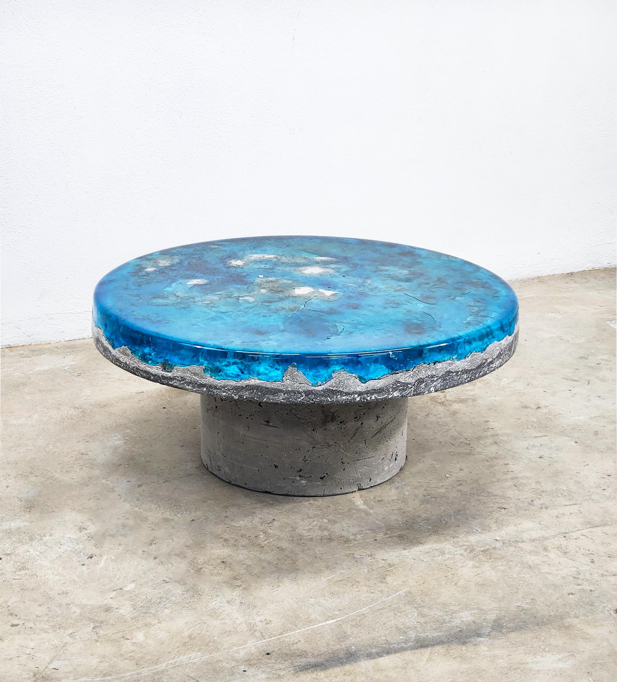 Introducing the TerraForma Coffee Table—a breathtaking union of artistry and form. Crafted from concrete and tinted resin, this masterpiece evokes the allure of the ocean floor. The concrete base boasts weathered textures, reminiscent of ancient