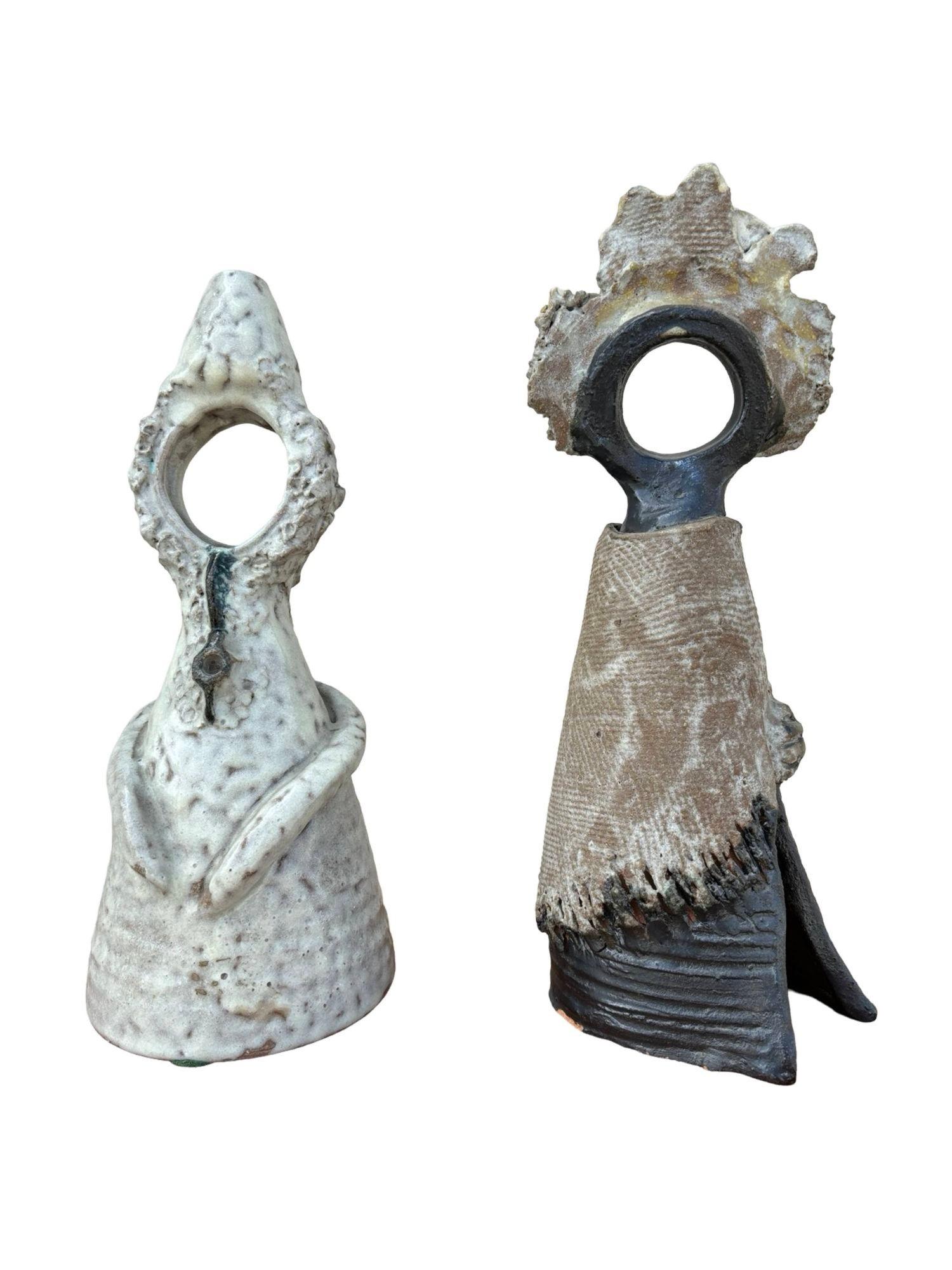 The male figure is cone-shaped, with arms gently cradling his hands to his stomach, embodying introspection. His surface features bold, abstract patterns and a glossy glaze.

The female figure, also cone-shaped, appears wrapped in a flowing dress or