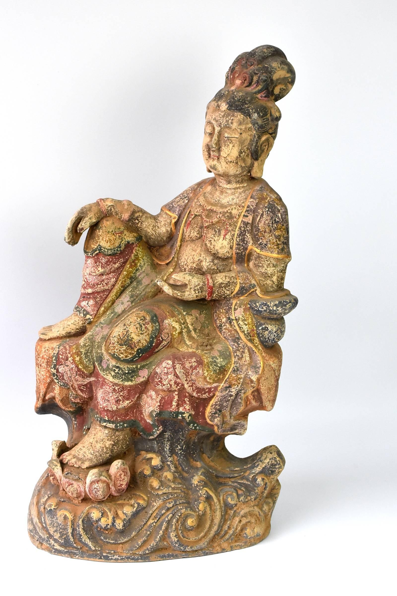 A fantastic terracotta piece featuring Bodhisattva Kwan Yin in a relaxed pose. Kwan Yin is the Goddess of Compassion, who takes away pain and blesses the devotees with good luck and great fortune. She is seated on a high pedestal with the ocean wave