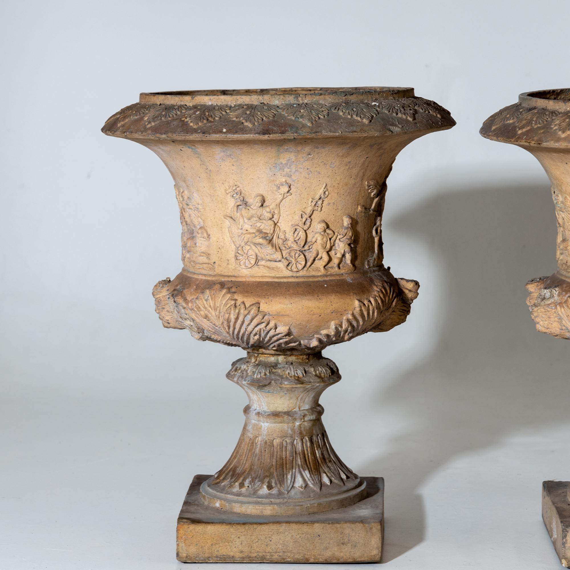 Pair of crater vases in the classicist style with figural scenes on the wall and square plinth. The vases are also decorated with acanthus leaves on the belly and on the rim. The side handles are missing and one vase has a crack. Signs of age and