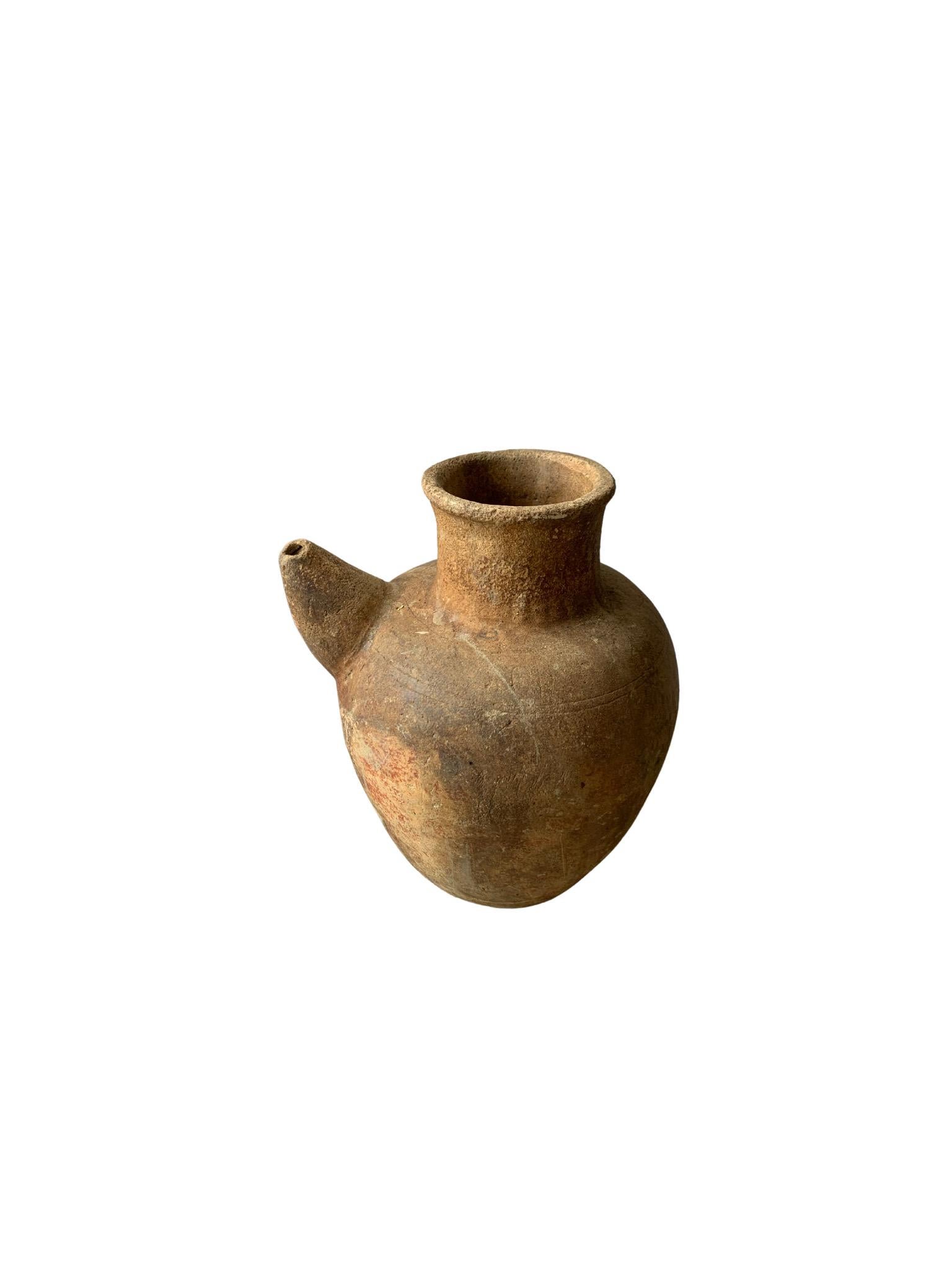 A terracotta jar from the island of Java, Indonesia with an elongated spout. Jugs such as these would have been used to store, water, oil and other liquids. The age related markings and fading to the jar add to its appeal. A versatile object to