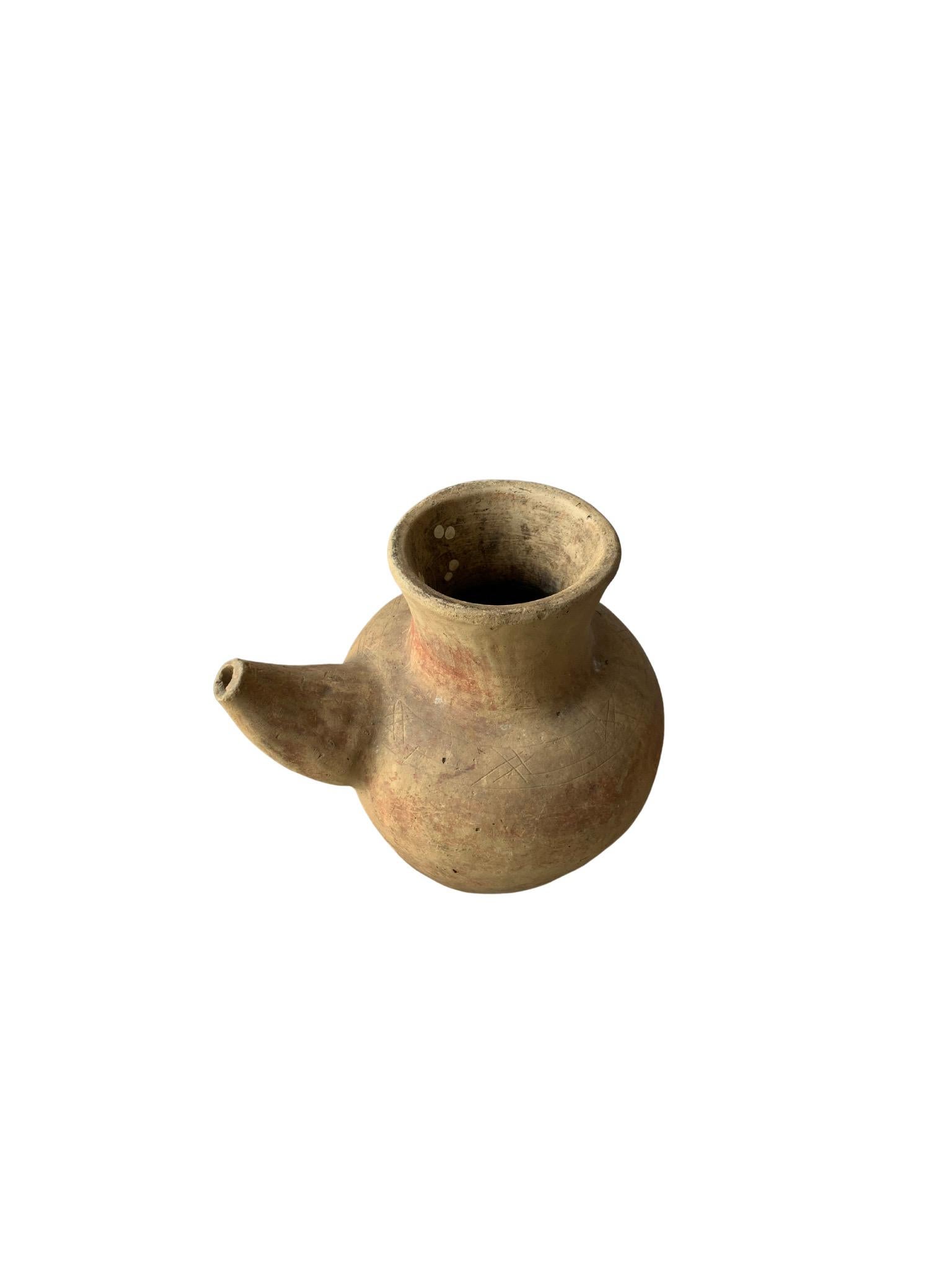 A terracotta jar from the island of Java, Indonesia with an elongated spout. Jugs such as these would have been used to store, water, oil and other liquids. The age related markings and fading to the jar add to its appeal. A versatile object to