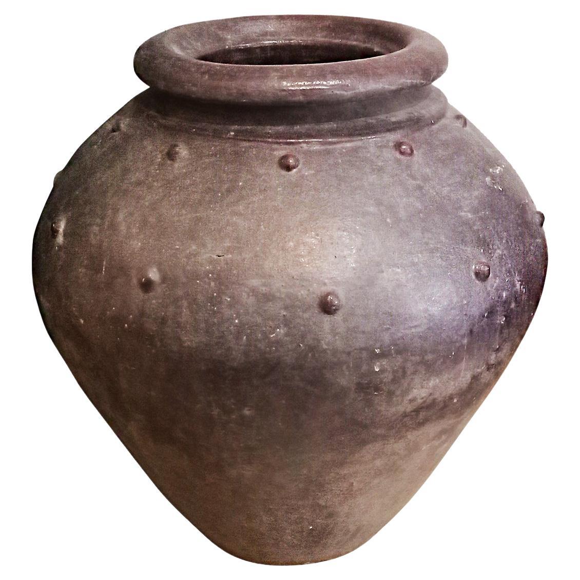 A large terracotta jar, hand-crafted in small, artisanal kilns in Bali, Indonesia. Glazed in burgundy color, with protruding decorative dots. Narrow top and bottom (11 inches), with 18 inches in total diameter and 19 inches high. 

The bottom has a