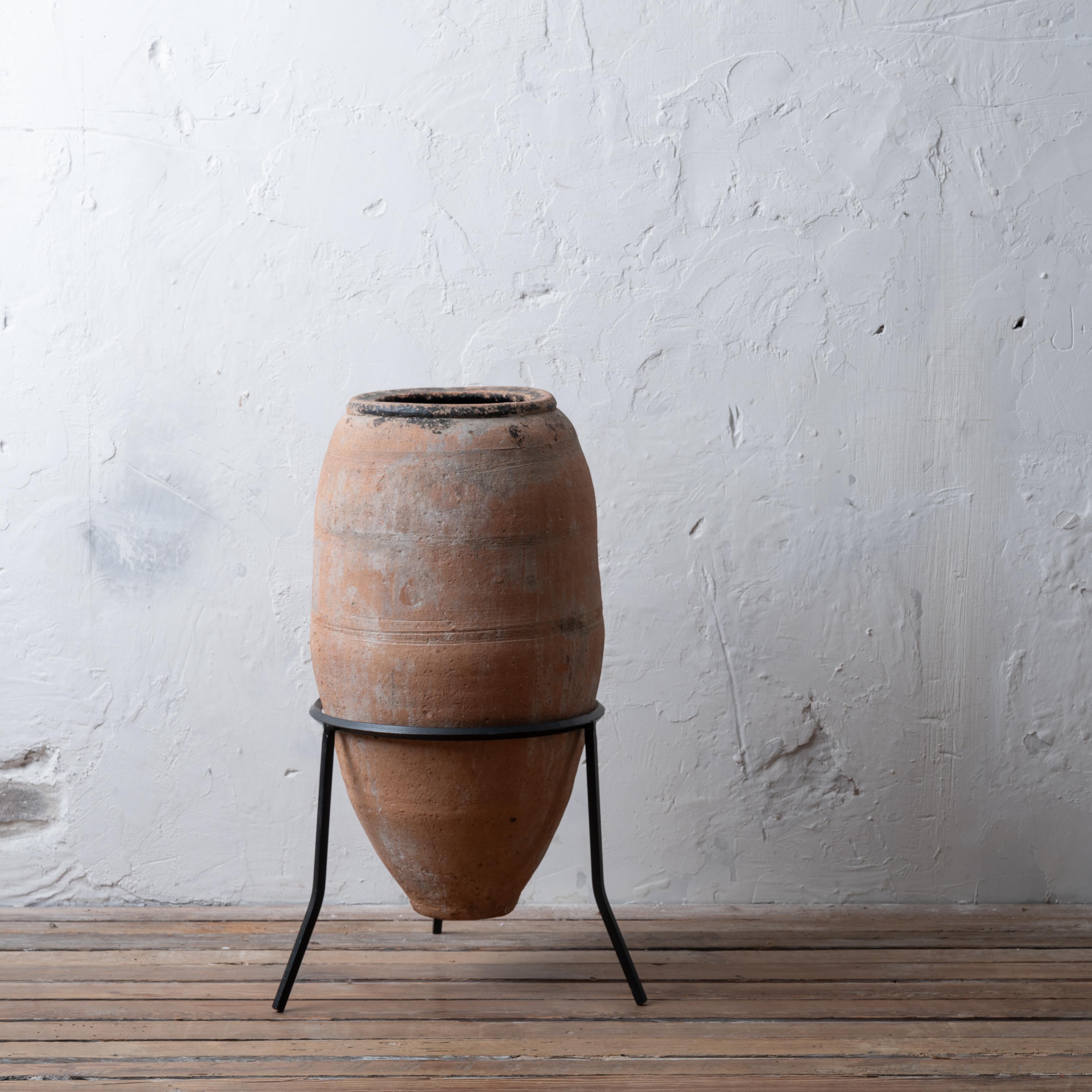 A mediterranean terracotta olive jar on later iron stand, 19th century.

15 inches wide by 31 inches tall; jar without stand 27 inches tall

