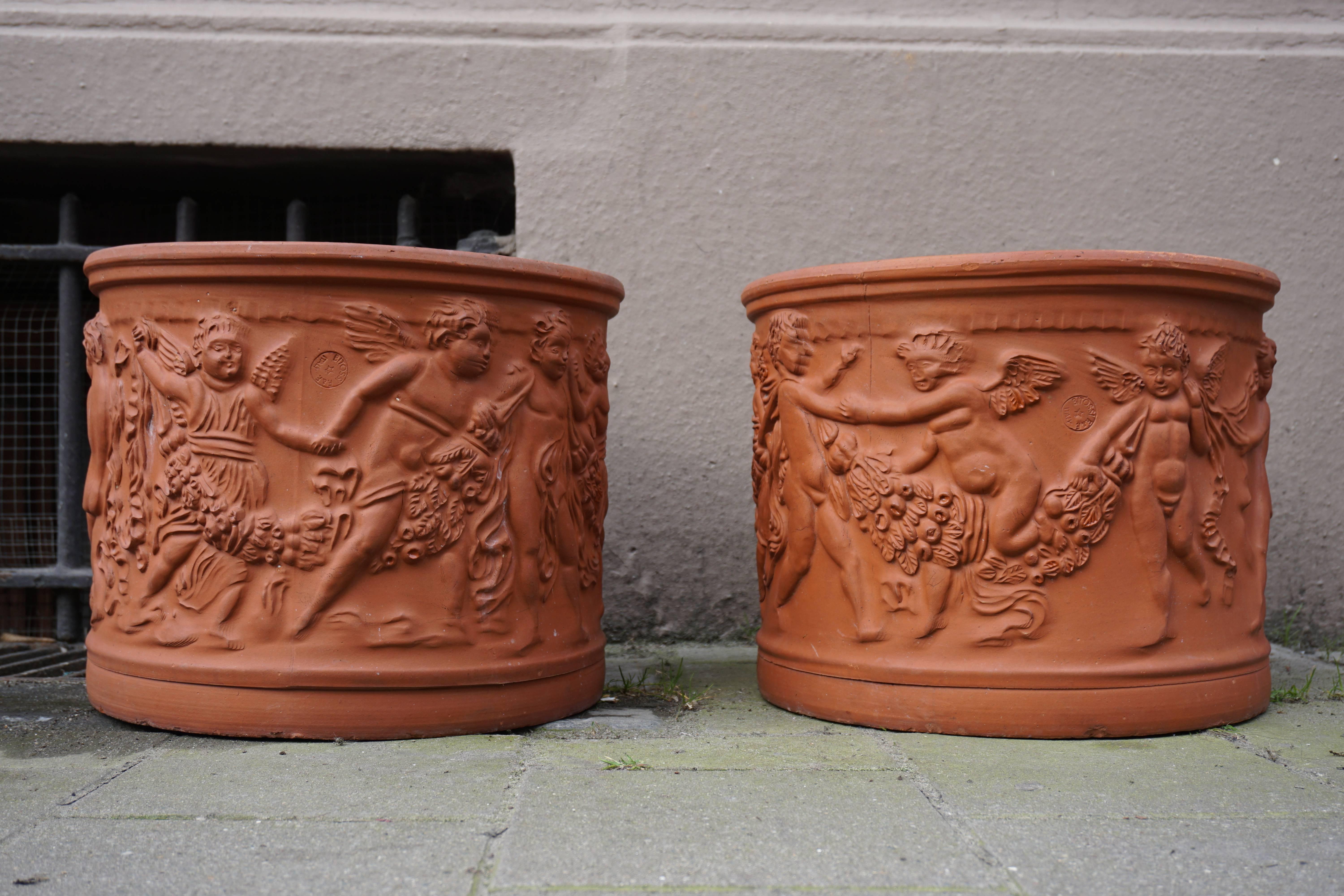 A pair of modern red terracotta planters stamped with the impressed mark of the famous Italian Bitossi manufactory, decorated with a continuous frieze of dancing putti carrying fruity festoons.