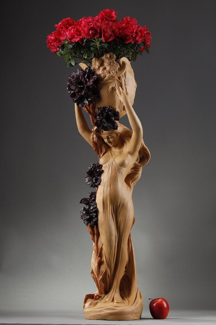 Important Art Nouveau sculpture in painted terracotta forming a cachepot. It represents a smiling woman wearing a flowing dress that uncovers her breasts, holding at arm's length a basket strewn with mauve flowers. A red ochre flowering branch runs