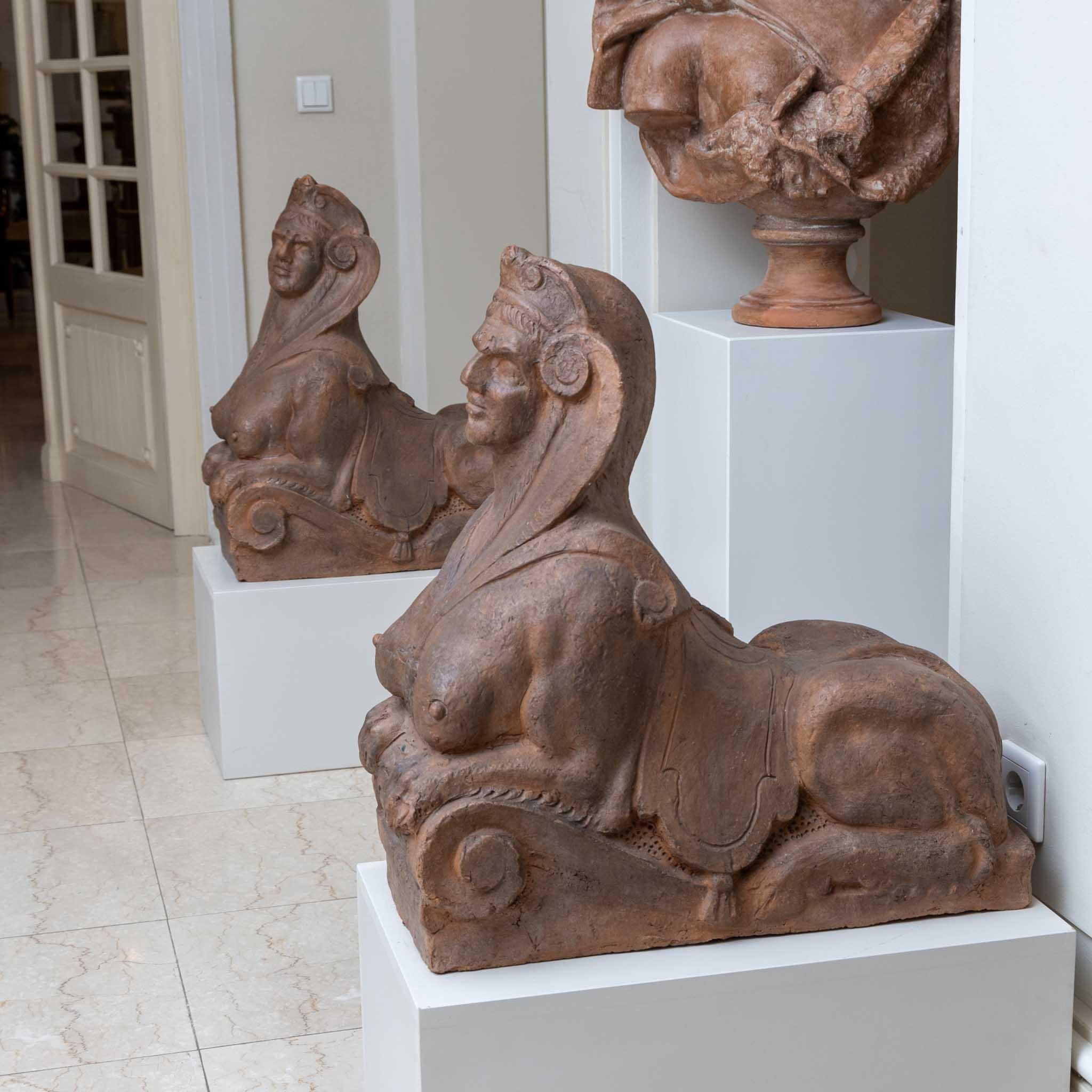 Pair of large, eroticized terracotta sphinxes, supporting their front legs on a large volute.